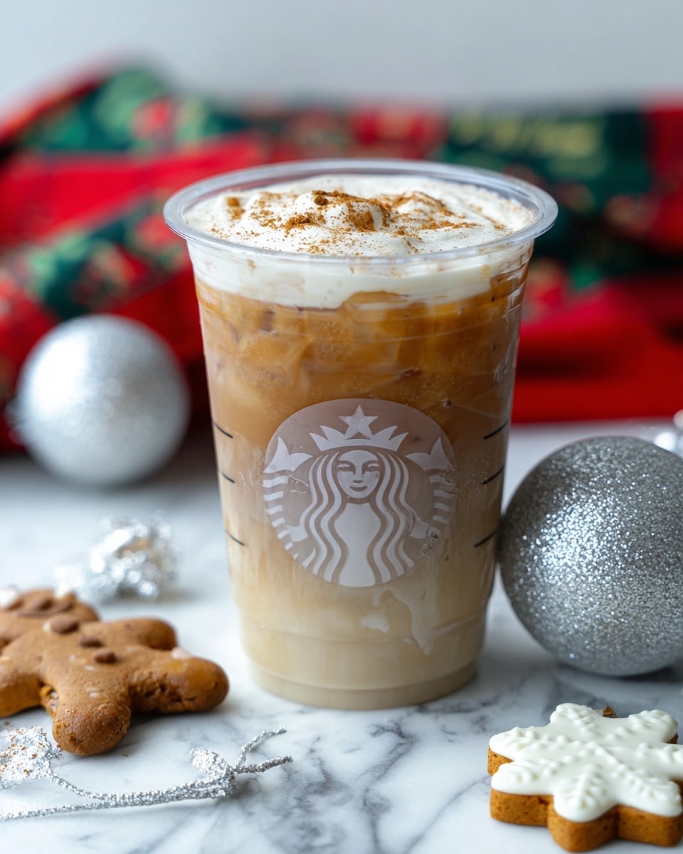 A clear plastic cup with a Starbucks logo holds a drink with three layers: the bottom layer is light brown and smooth, the middle layer is a lighter creamy beige with a mix of ice visible, and the top layer is white foam sprinkled with cinnamon. The cup is placed on a white marbled surface with holiday decorations around, including a silver glittery ornament, a silver jingle bell, a gingerbread cookie, and a white felt snowflake. In the background, there is a blurred red and green patterned cloth. Photo taken with an iphone --ar 4:5 --v 7