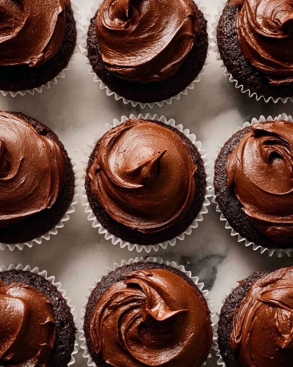 The image shows a close-up of nine chocolate cupcakes in white paper liners arranged tightly on a white marbled surface. Each cupcake has one thick layer of smooth, rich dark brown chocolate frosting on top with visible swirled textures and soft peaks, giving a glossy and creamy look. The cupcakes are uniform in size and evenly spaced, filling the frame with a warm, inviting appearance. photo taken with an iphone --ar 4:5 --v 7