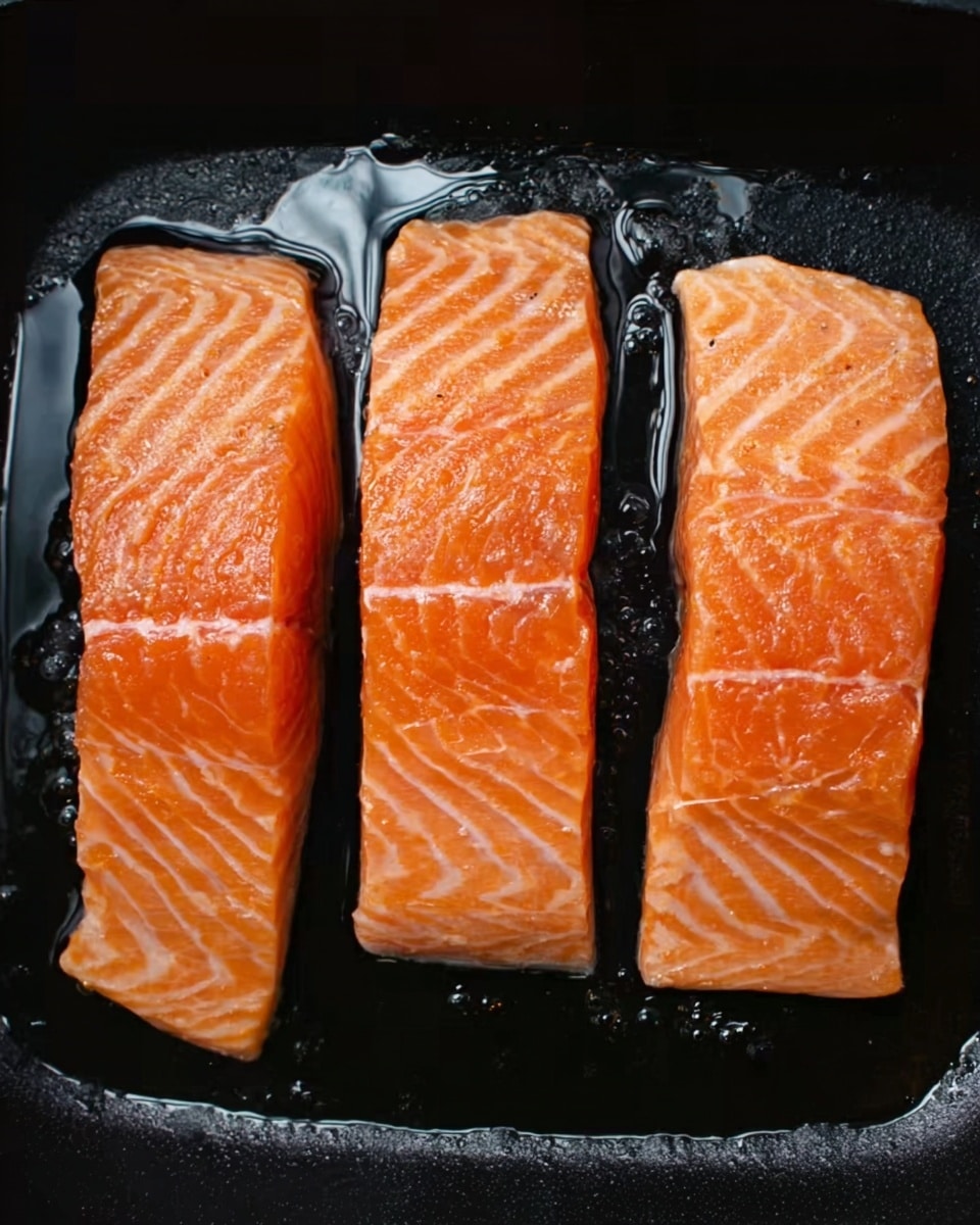 The image shows three raw, light orange salmon fillets with white stripes lying side by side inside a black pan. The fillets have a smooth, slightly shiny texture with visible natural patterns in the fish. The pan holds some clear, oily liquid around the edges, adding a slight glisten to the scene. The black background of the pan provides a strong contrast to the bright salmon. photo taken with an iphone --ar 4:5 --v 7