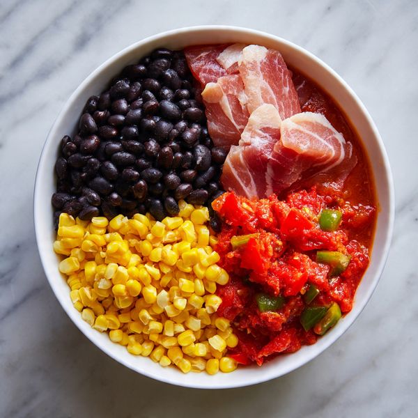 A white bowl is filled with four main sections: a large, smooth, pale piece of raw meat on the right, a shiny pile of black beans in the upper left, bright yellow corn kernels densely packed in the lower left, and a chunky mix of red diced tomatoes with small bits of green pepper in the lower right. The ingredients sit side by side on a base of reddish sauce and the bowl is placed on a white marbled surface. Photo taken with an iphone --ar 4:5 --v 7