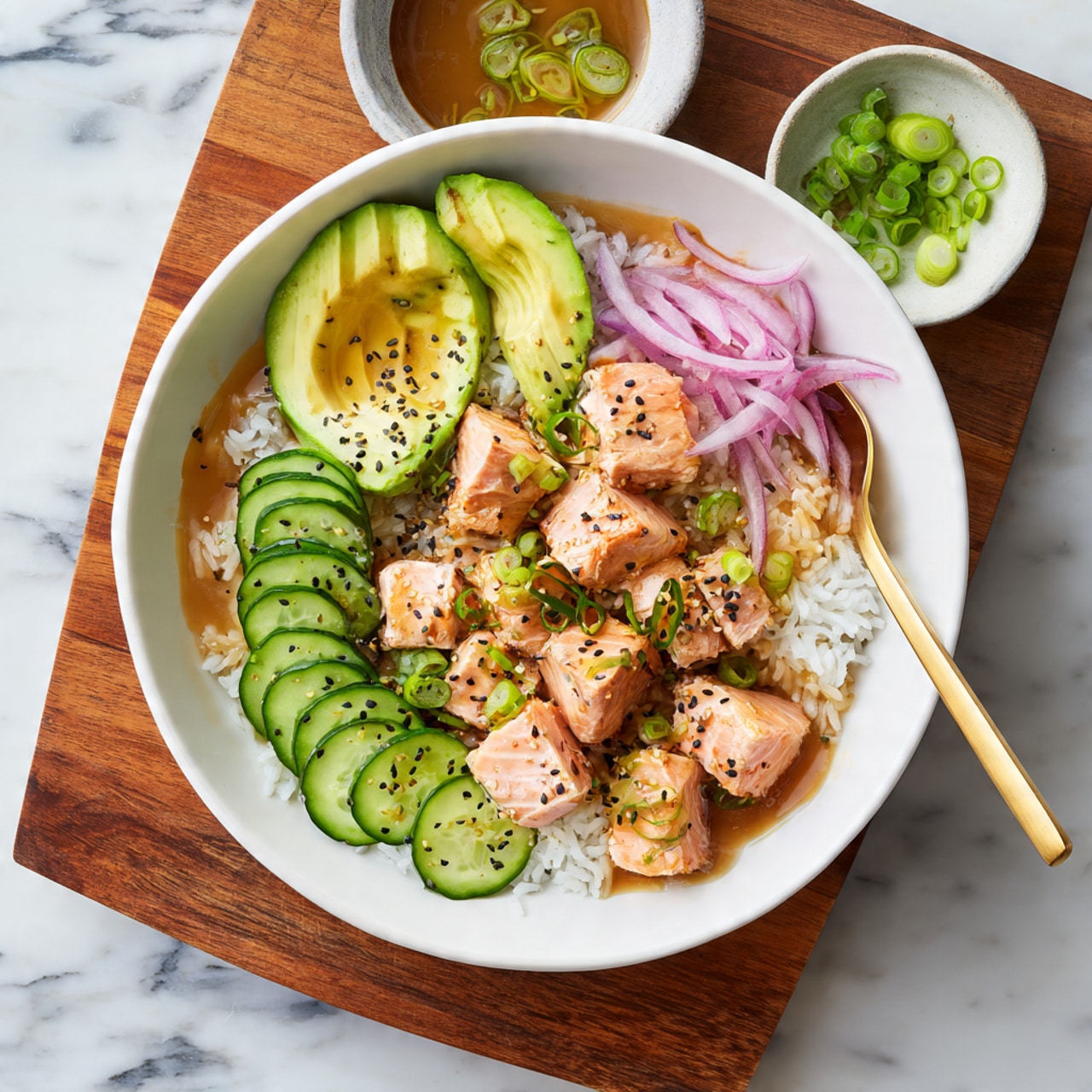A white bowl filled with a layer of white rice at the bottom, topped with slices of green cucumber arranged on one side and chunks of grilled salmon with a slightly browned surface piled in the center. Bright green avocado pieces are placed around the edges, along with thin rings of pink-red onion scattered on top. The dish is drizzled with a light brown sauce and sprinkled with black sesame seeds and slices of green onion, with a gold spoon resting inside the bowl. The bowl sits on a wooden board with small bowls of sliced green onion and more pink-red onion nearby, all set on a white marbled surface. Photo taken with an iphone --ar 4:5 --v 7