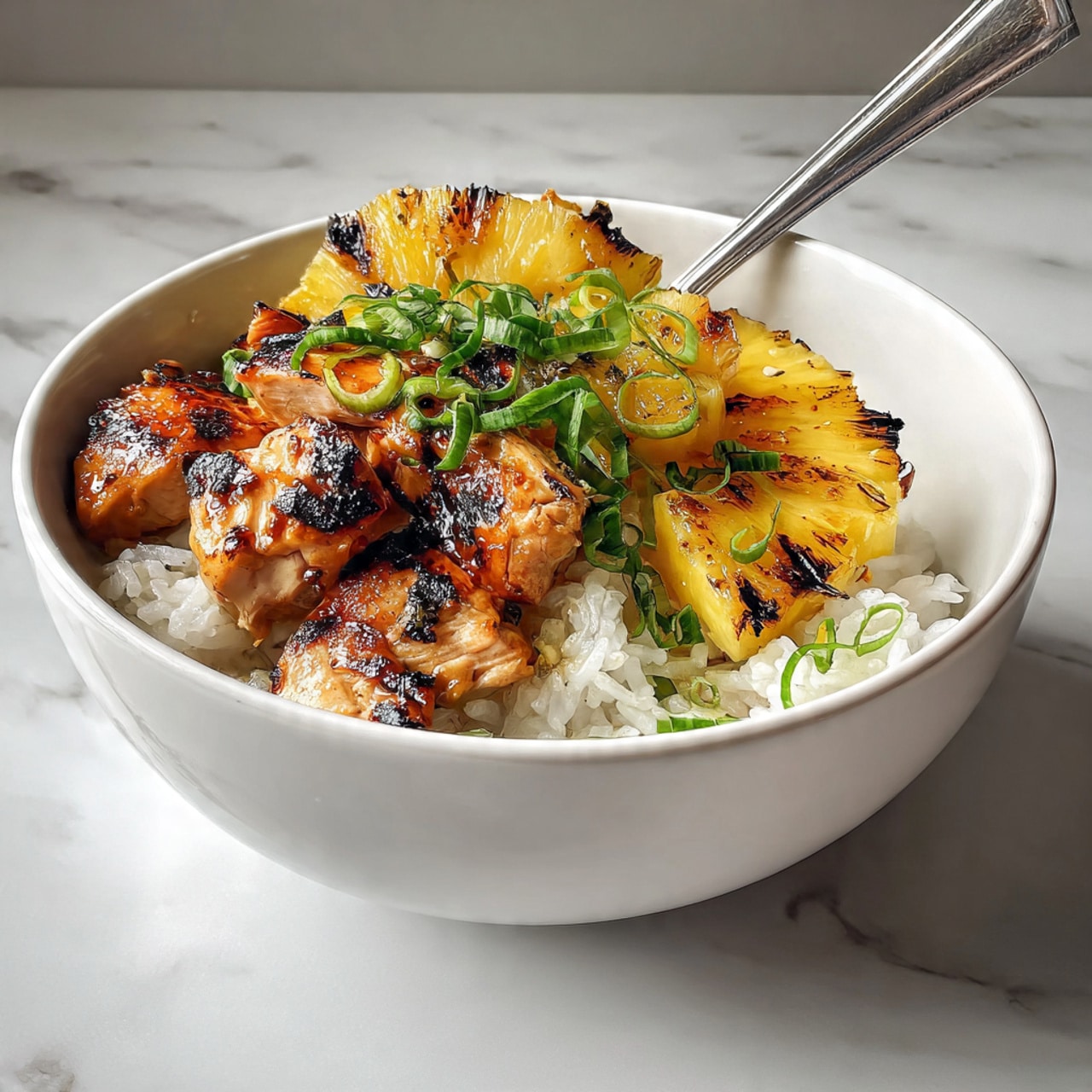 A white bowl holds three layers: the bottom is a bed of fluffy white rice, soft and slightly clumped; on top of the rice, there are three thick, grilled pineapple rings with bright yellow color and visible charred grill marks in dark brown; next to the pineapple, there are several pieces of grilled chicken thighs with a glazed, shiny orange-brown color and dark brown grill marks, garnished with small chopped green onions scattered on both the chicken and rice. A silver fork rests on the rice near the chicken, and the entire scene sits on a white marbled surface. Photo taken with an iphone --ar 4:5 --v 7