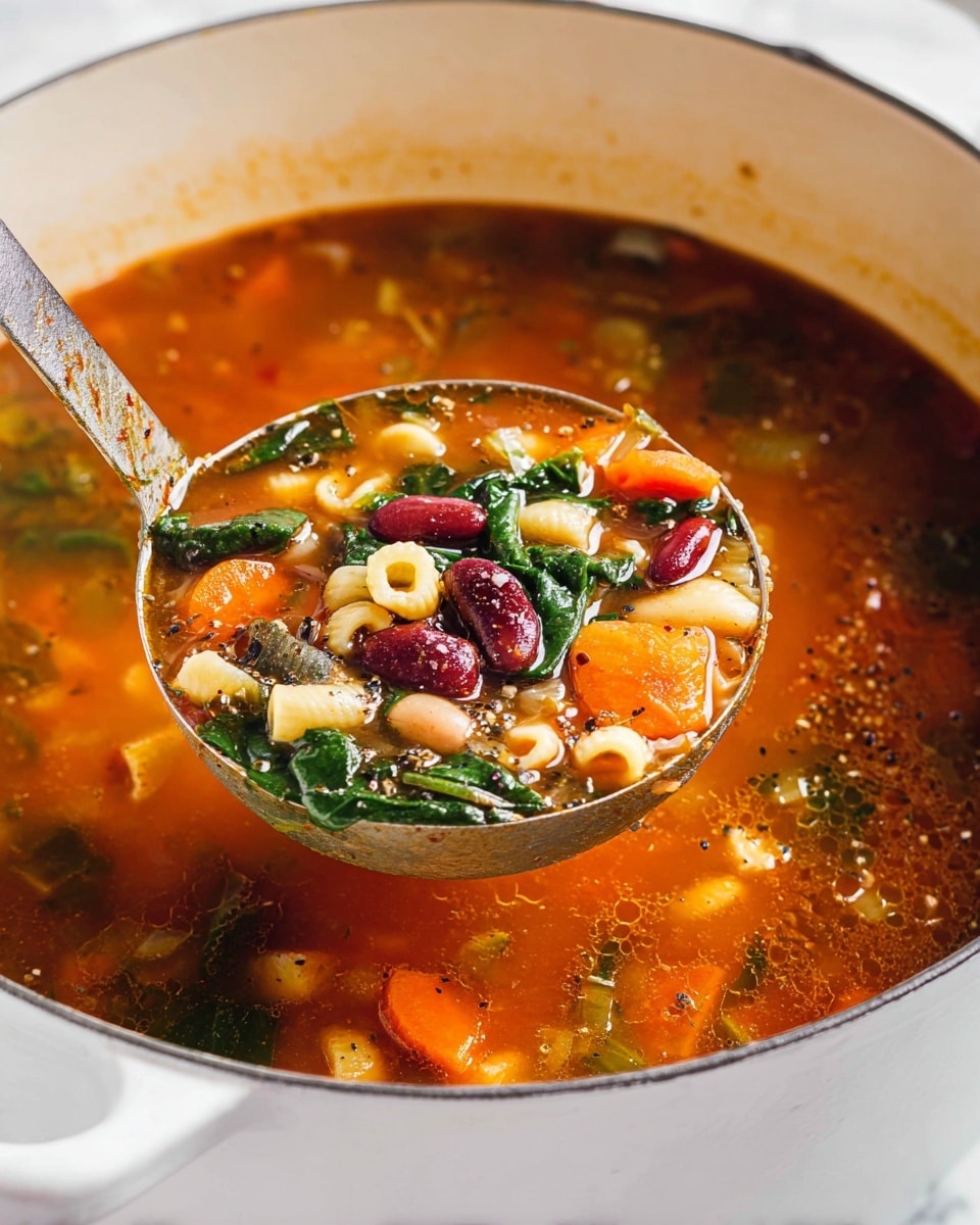A ladle full of vegetable soup is lifted from a white pot sitting on a white marbled texture. The soup has a deep orange-red broth with visible layers of ingredients: green leafy spinach, dark red kidney beans, small white beans, small pasta shells, and diced orange carrots. The broth is liquid with floating herbs and spices, and there is a sprinkle of black pepper on the soup's surface and ingredients. The ladle is metal and slightly worn, shining against the colors of the soup. photo taken with an iphone --ar 4:5 --v 7