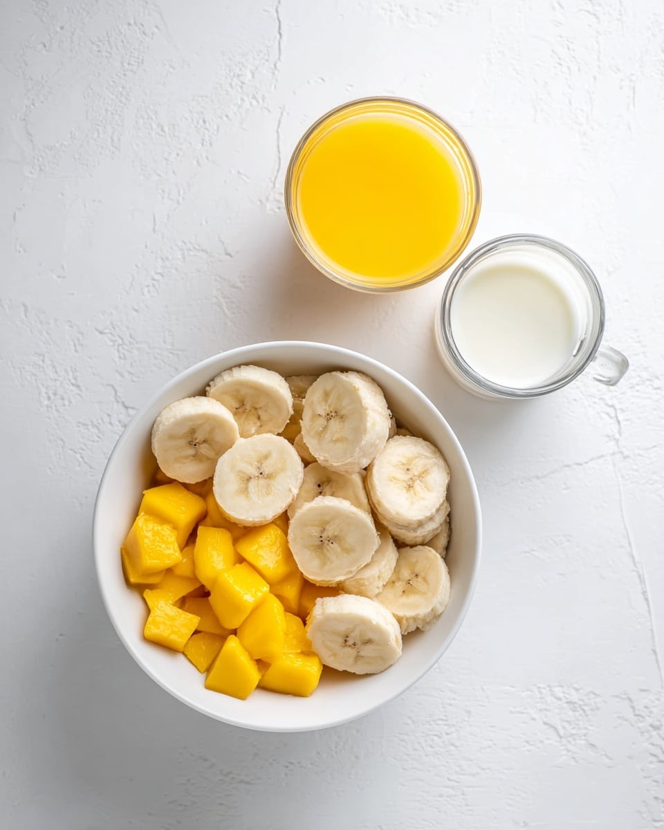 A white bowl filled with two layers: the bottom layer contains bright yellow frozen mango chunks, and the top layer has light beige banana slices arranged in a circular pattern. Nearby are three small clear containers placed on a white marbled surface: one filled with smooth bright yellow juice, one with creamy white yogurt, and one with slightly off-white milk. The scene is bright and clean with soft natural light. photo taken with an iphone --ar 4:5 --v 7