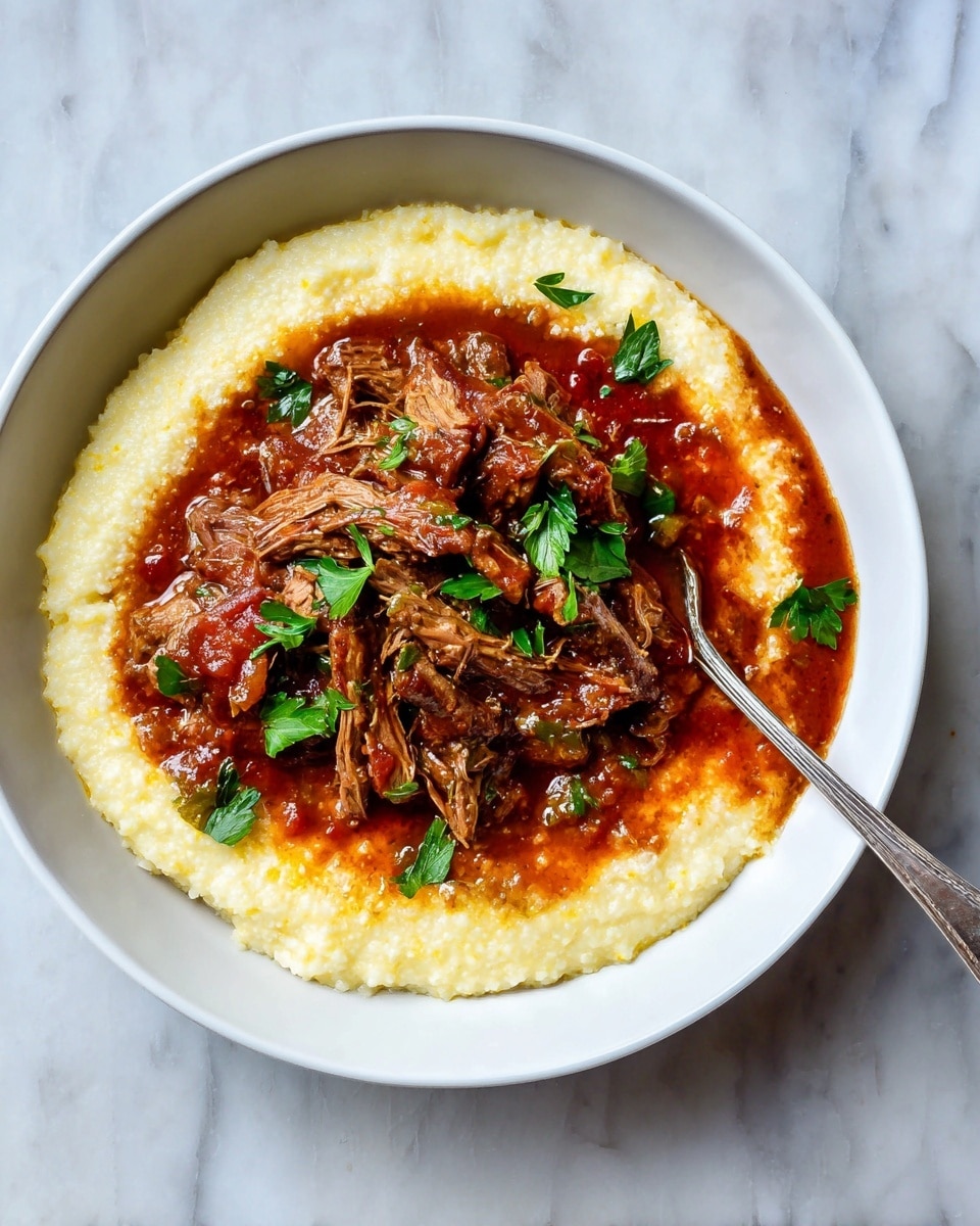 A white bowl on a white marbled surface holds three main layers: the bottom layer is creamy, pale yellow grits with a smooth and slightly grainy texture, spread out in a ring around the edge of the bowl. The middle layer is a rich, thick red-brown sauce with visible chunks of soft vegetables, filling the center and edges inside the grits ring. On top, shredded brown meat is placed in the center, covered with some of the sauce and garnished with green parsley leaves. A silver fork rests inside the bowl on the right side, touching the food. photo taken with an iphone --ar 4:5 --v 7