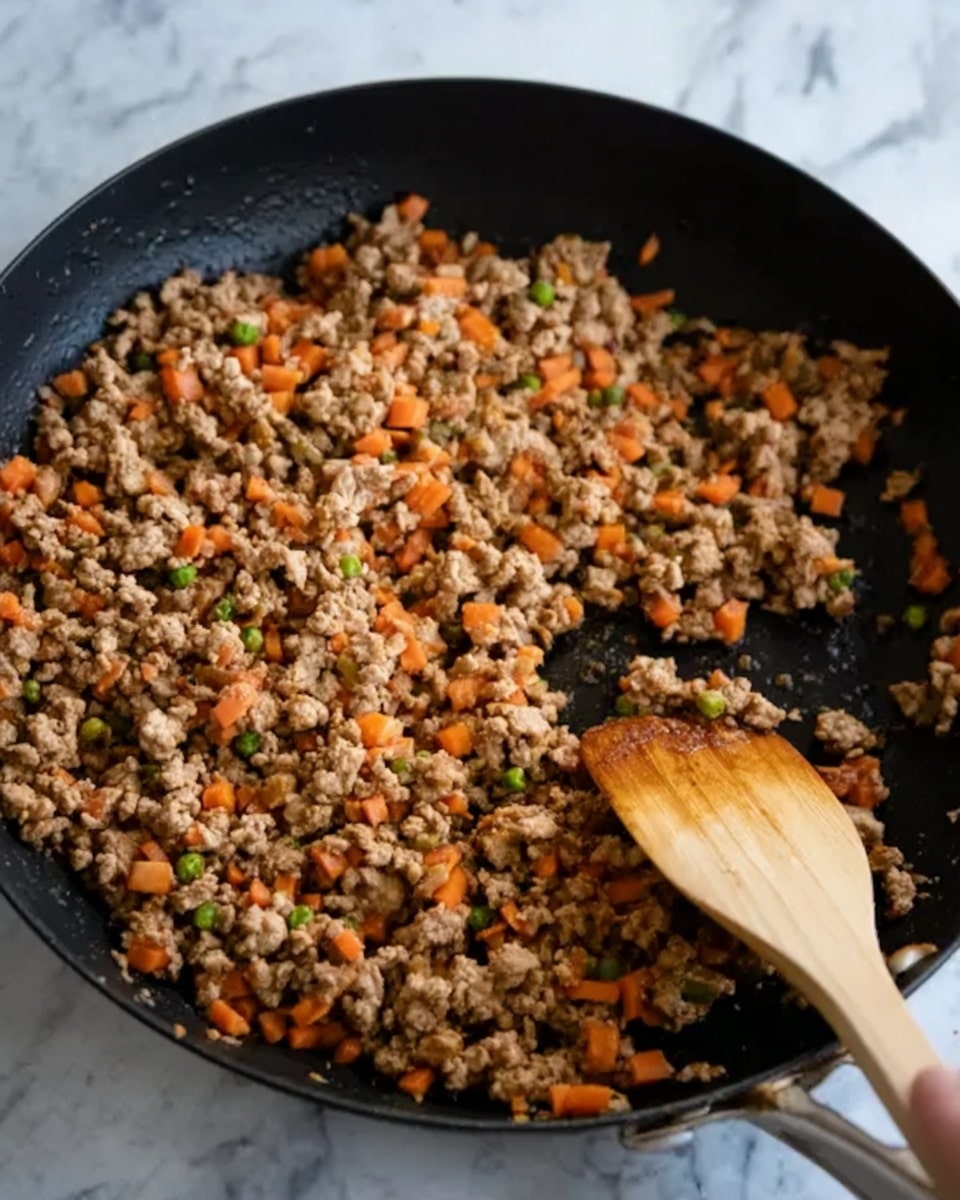In the image, there is a black skillet filled with cooked ground meat mixed with small pieces of orange carrots and green peas. The meat looks crumbly and browned evenly, and the vegetables add some bright color. A wooden spatula is stirring the mixture, held by a woman's hand, which is partially visible at the top right corner. The background shows a white marbled surface. Photo taken with an iphone --ar 4:5 --v 7