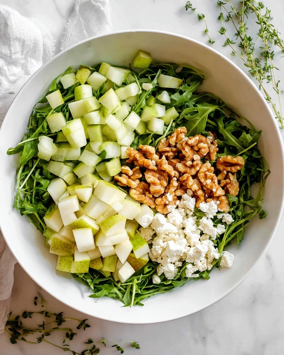 A white bowl is filled with fresh green arugula leaves forming the base layer. On top, there is a layer of small chopped light green and white pear cubes piled on one side. Next to the pears, there are golden-brown walnut pieces spread in a small pile. On the opposite side, there is a scattering of white crumbly cheese that contrasts with the green arugula. The bowl sits on a white marbled surface with small sprigs of green herbs scattered around. Photo taken with an iphone --ar 4:5 --v 7