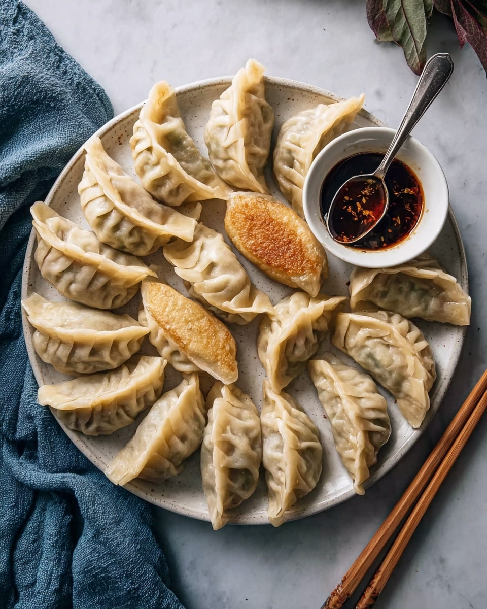 A round white plate holds about sixteen dumplings arranged close together, each wrapped in a pale dough with visible pleated folds, showing a slightly translucent texture revealing a hint of the filling inside. Most dumplings are steamed and light beige, but one dumpling in the center is golden brown and fried with a crispy texture. To the top right of the plate is a small white bowl filled with dark brown sauce, rich and shiny, and a silver spoon resting inside. A pair of wooden chopsticks lies diagonally to the right side of the plate, resting on the white marbled surface. A blue cloth napkin is partially visible on the bottom left corner of the image. Photo taken with an iphone --ar 4:5 --v 7