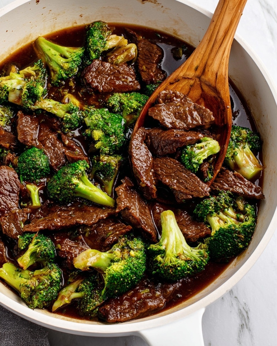 The image shows a white pan filled with beef and broccoli stir-fry. The dark brown beef slices are tender and cooked, sitting in a rich, glossy brown sauce that coats the pieces. Bright green broccoli florets are mixed evenly throughout, with some pieces showing slight charring for added texture. A wooden spoon is lifting some beef slices and broccoli from the pan, with the handle resting on the right side. The pan is placed on a white marbled surface. photo taken with an iphone --ar 4:5 --v 7