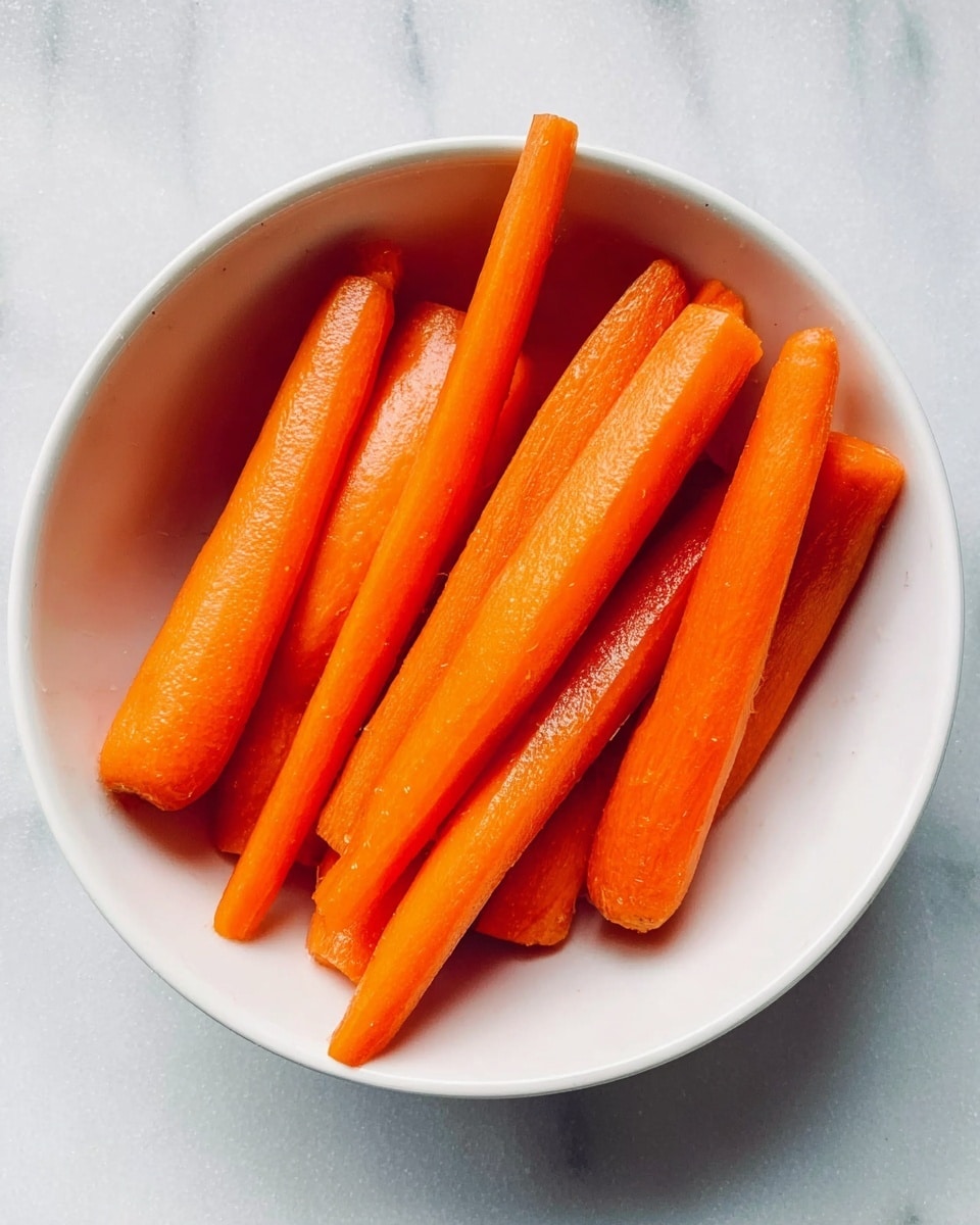 A white bowl filled with eight whole bright orange peeled carrots. The carrots are smooth and shiny, lying in different directions but mostly parallel. The bowl is sitting on a white marbled surface. photo taken with an iphone --ar 4:5 --v 7