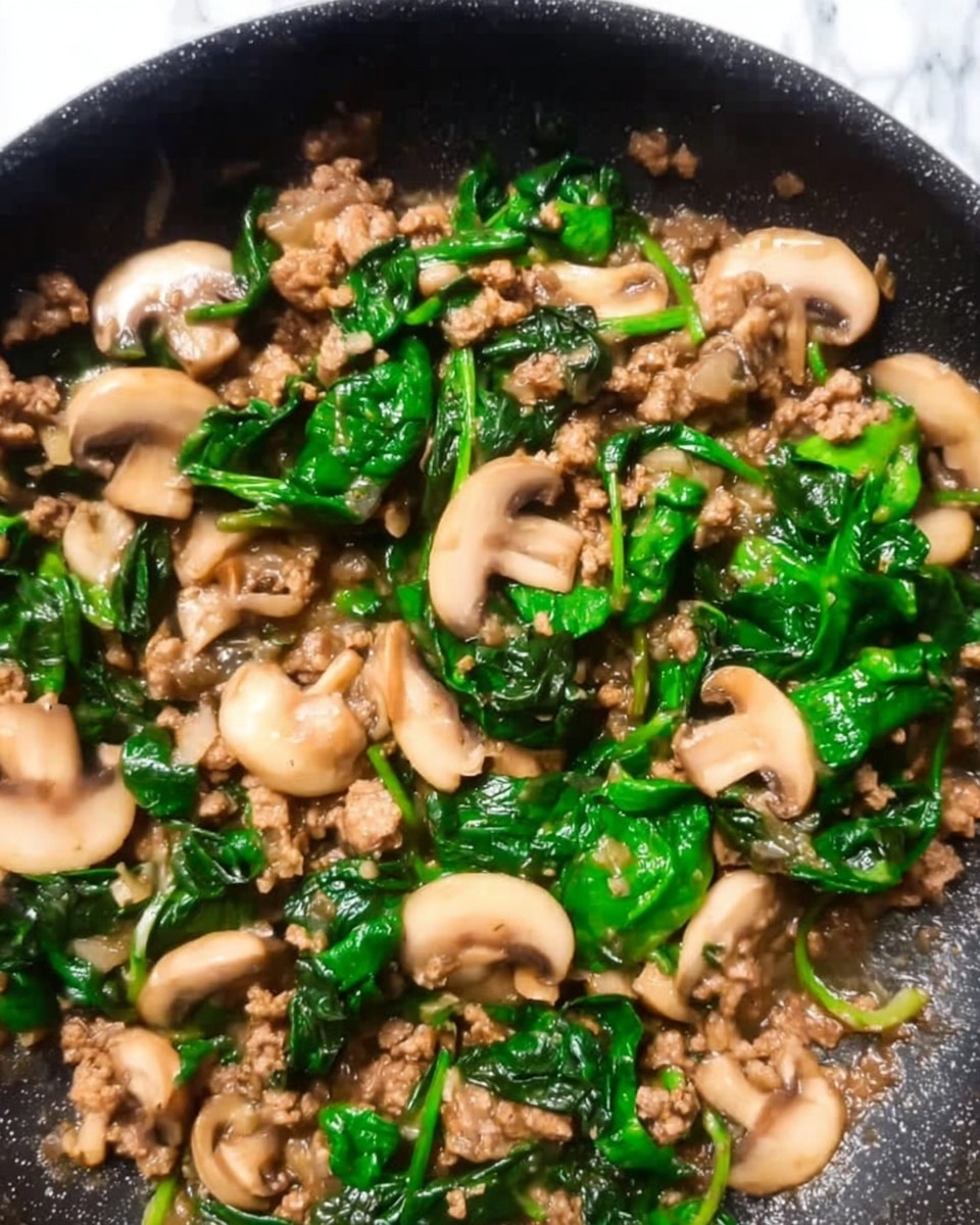 The image shows a close-up of a cooked dish in a dark pan, featuring three main layers: at the bottom, soft brown ground meat with a slightly crumbly texture; on top, fresh bright green spinach leaves that appear wilted but still vibrant; scattered throughout are light beige sliced mushrooms with a smooth, shiny surface. The ingredients are mixed and cooked together, creating a colorful blend of green, brown, and beige against the black pan, with some visible sauce coating the food, all set against a white marbled background. photo taken with an iphone --ar 4:5 --v 7