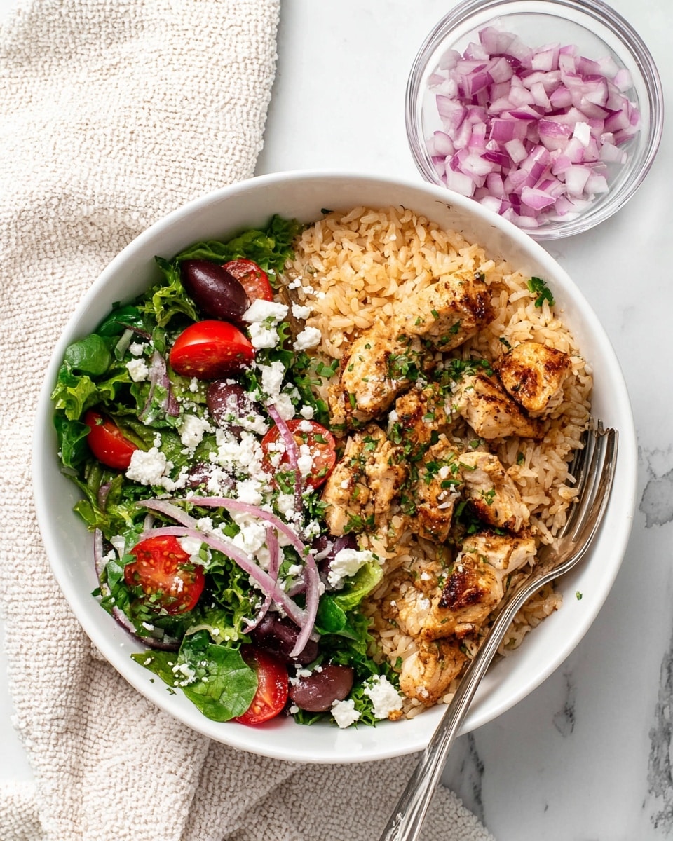 A white bowl filled with two main parts: on the right side, light brown cooked rice mixed with small pieces of grilled chicken that have a golden-brown sear, sprinkled lightly with white crumbled cheese and small green herbs; on the left side, a fresh salad made of dark green mixed leaves, red cherry tomato halves, purple olives, thin light purple onion rings, and more white cheese crumbs scattered on top. A silver fork rests on the right edge of the bowl, partly in the rice. Above the bowl, a small clear round bowl with chopped red onions sits on a white marbled surface, next to a cream-colored textured cloth. Photo taken with an iphone --ar 4:5 --v 7