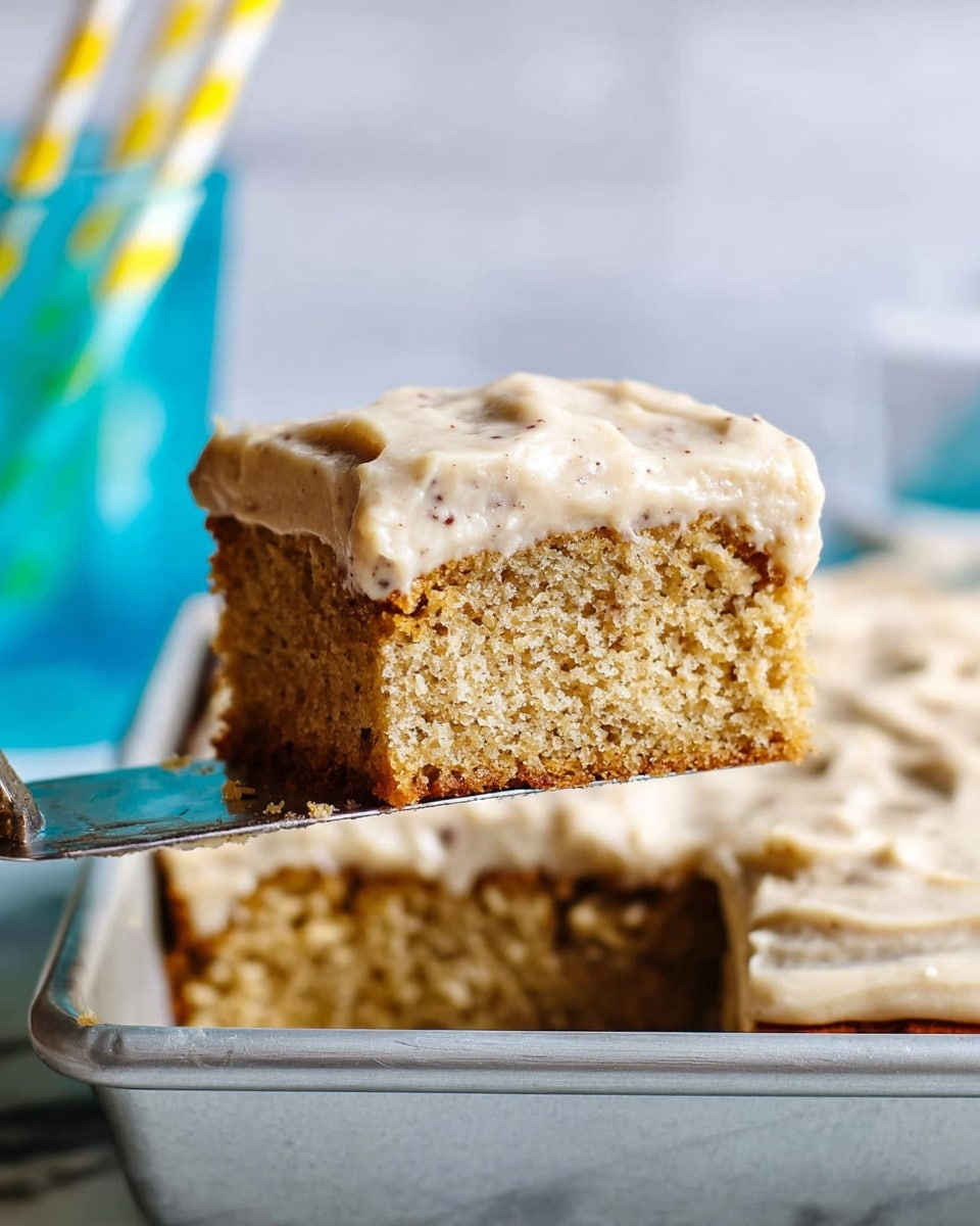 A close-up of a thick square slice of light brown cake with small dark specks inside, lifted by a metal spatula over a rectangular metal pan with the rest of the cake below. The cake has two layers: the bottom layer is soft and spongy with a golden-brown edge, and the top layer is a creamy, light beige frosting spread unevenly with a smooth texture. The background shows a white marbled surface and blurry blue glass with yellow and white striped straws. Photo taken with an iphone --ar 4:5 --v 7