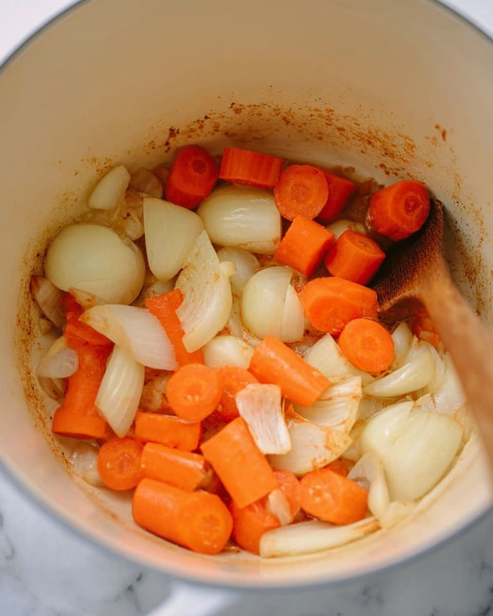 Inside a white pot, there are several pieces of onion and carrot cooking. The onions are light yellow with some parts slightly brown from cooking and are cut into medium chunks. The carrots are bright orange and sliced into thick round pieces. The white pot shows some brown spots on the sides, with a wooden spoon on the right slightly stirring the vegetables. The background is a white marbled texture. photo taken with an iphone --ar 4:5 --v 7