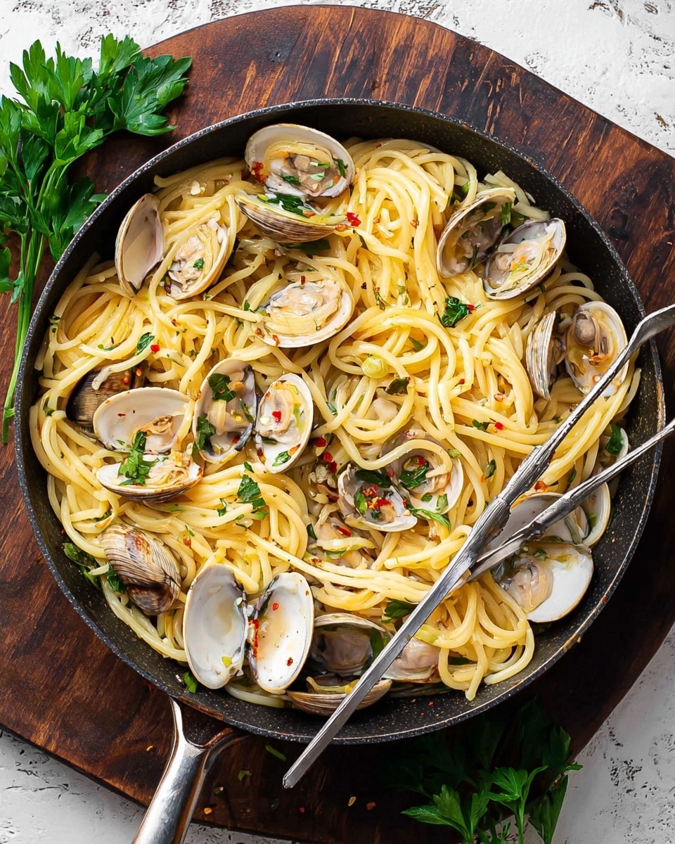 A black pan is filled with long yellow spaghetti noodles mixed with light brown and white clams in open shells scattered throughout. The noodles are coated in a light, glossy sauce with specks of red flakes, and there are some green parsley leaves placed on top adding a fresh touch. Two silver forks rest inside the pan, with their handles leaning to the right. The pan sits on a rustic wooden surface with a bunch of fresh green parsley at the top left corner. Photo taken with an iphone --ar 4:5 --v 7