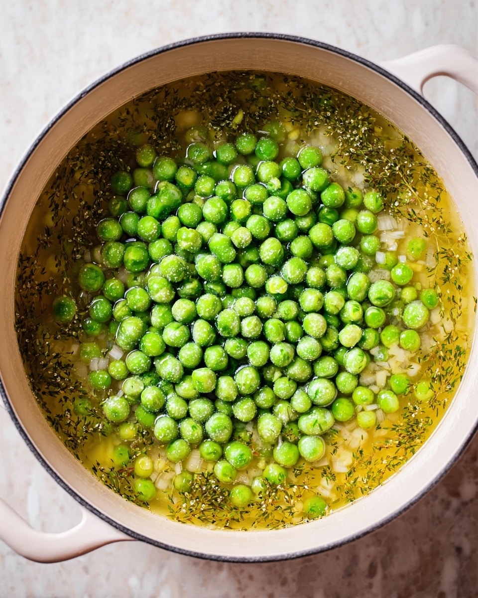 A white pot filled with a broth that is light golden yellow with hints of green herbs floating within. On top, there is a large mound of frozen green peas, round and dry with a frosty texture, sitting in the center of the broth. Small pieces of onion and herbs are slightly visible through the clear liquid beneath the pile of peas. The pot is placed on a white marbled surface. photo taken with an iphone --ar 4:5 --v 7