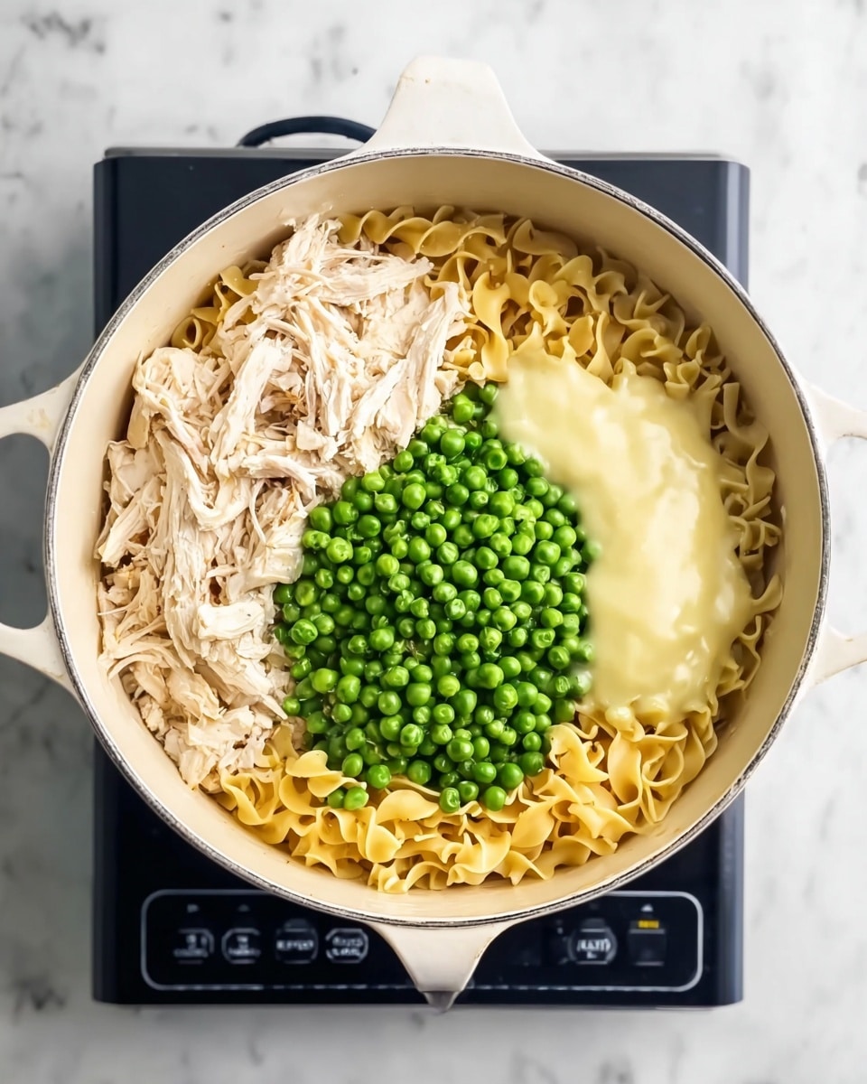 A white pot is filled with three main layers arranged side by side on top of egg noodles, which are golden yellow and slightly curled. On the left side, there is a layer of shredded light beige cooked chicken. The middle section is covered with a mound of small, round bright green frozen peas. On the right side, a smooth, creamy light yellow sauce rests on top of the noodles. The pot is placed on a black electric stove with digital controls, all set against a white marbled surface. photo taken with an iphone --ar 4:5 --v 7