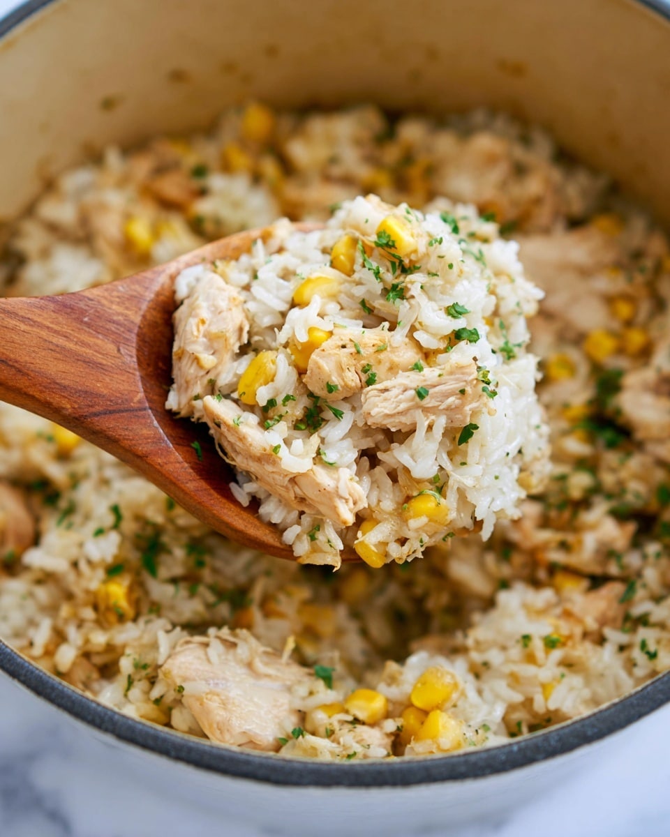 A close-up view of a pot filled with a cooked rice dish that has three main layers: soft beige pieces of cooked chicken with some herbs sprinkled on top, mixed evenly with white rice grains showing a slightly sticky texture, and bright yellow corn kernels adding small pops of color throughout. There are also small green chopped herbs scattered on top and mixed in. A wooden spoon lifts a scoop from the pot, showing a balanced mix of the ingredients. The background is white marbled texture. Photo taken with an iphone --ar 4:5 --v 7