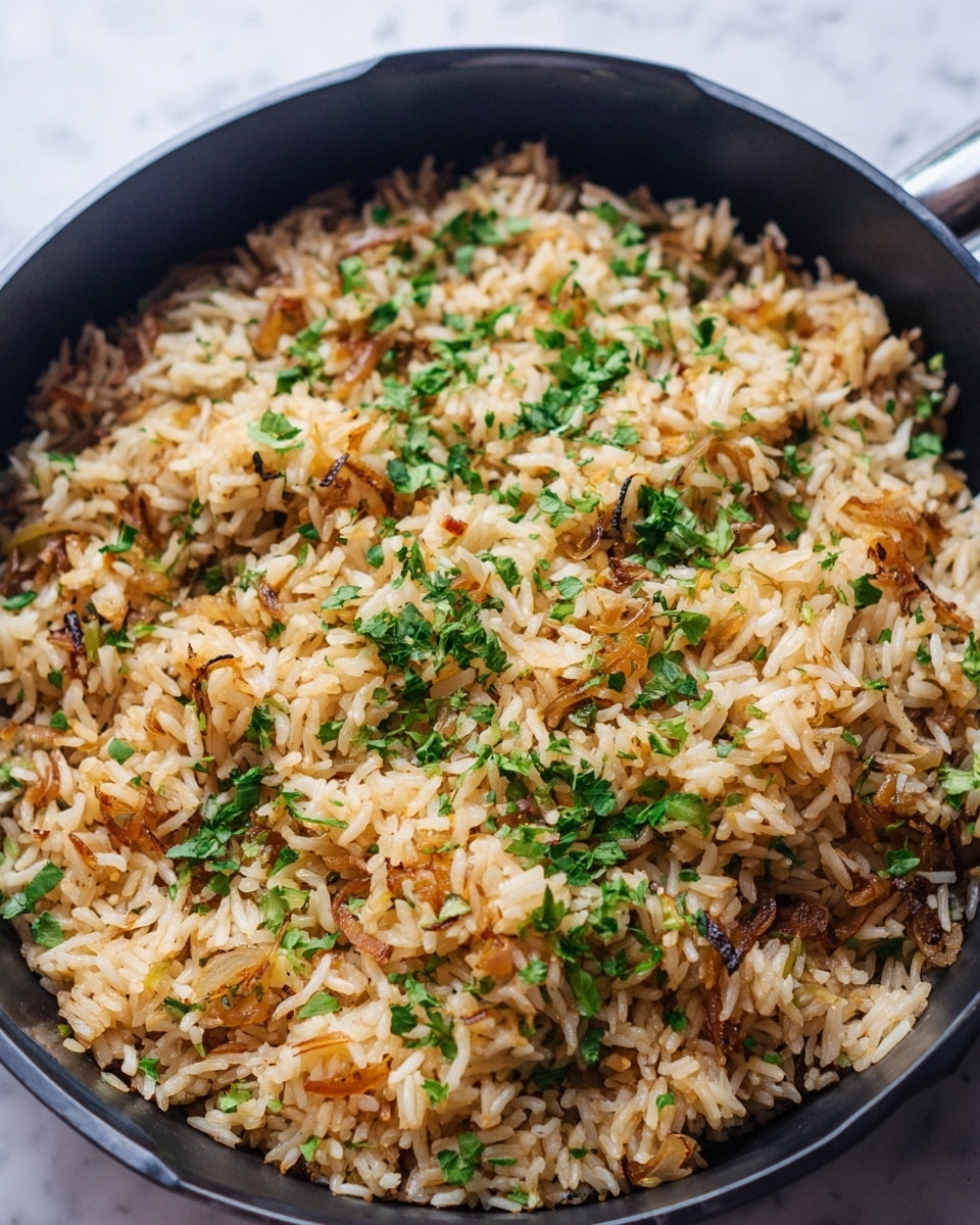 A close-up view of a black pan filled with golden cooked rice mixed with small pieces of browned onions and scattered finely chopped green herbs on top. The rice grains have a fluffy texture with a mix of light brown and white colors, and the green herbs add a fresh contrast. The pan sits against a white marbled textured surface. photo taken with an iphone --ar 4:5 --v 7