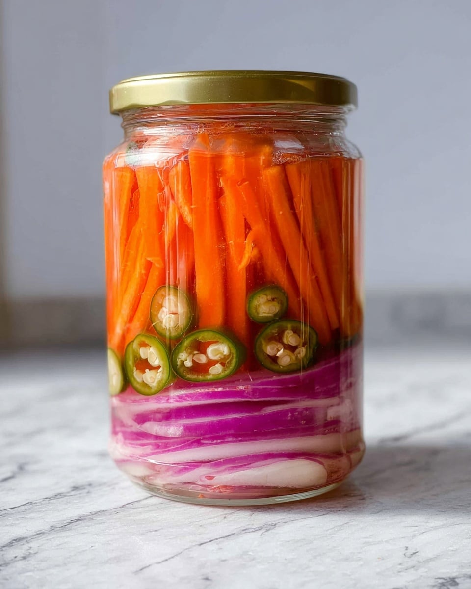 The image shows a clear glass jar filled with three visible layers of pickled vegetables. At the bottom are thick slices of red onion mixed with round slices of green chili, showing a mix of white, purple, and green tones. Above this is a large layer of thin, bright orange carrot sticks packed tightly. The jar has a golden lid and is placed on a white marbled surface with a blurred light background. The vibrant colors and textures of the vegetables are clear through the glass. Photo taken with an iphone --ar 4:5 --v 7