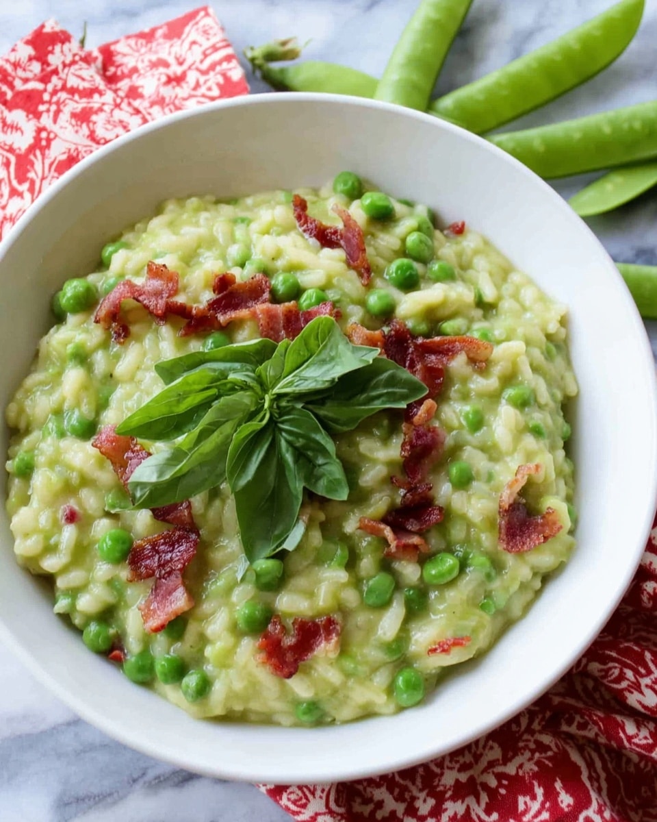 A white bowl is filled with a creamy green risotto that looks soft in texture. Inside the risotto, there are small green peas scattered throughout along with thin strips of reddish-brown bacon. On top of the risotto, there is a small bunch of fresh dark green basil leaves adding color contrast. The bowl sits on a white marbled surface with fresh pea pods and green leaves arranged nearby, and a red and white patterned cloth partly visible underneath the bowl. Photo taken with an iphone --ar 4:5 --v 7