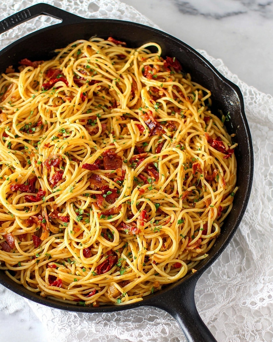 The image shows a black cast iron skillet filled with cooked spaghetti mixed with small red chunks of sun-dried tomatoes and bits of cured meat. The pasta is golden brown with some darker browned spots and is sprinkled with finely chopped green herbs. The skillet rests on a white marbled surface with a white lace cloth partially visible beneath it. The spaghetti strands are loosely layered, creating a textured and slightly glossy appearance from the sauce and oil used. Photo taken with an iphone --ar 4:5 --v 7