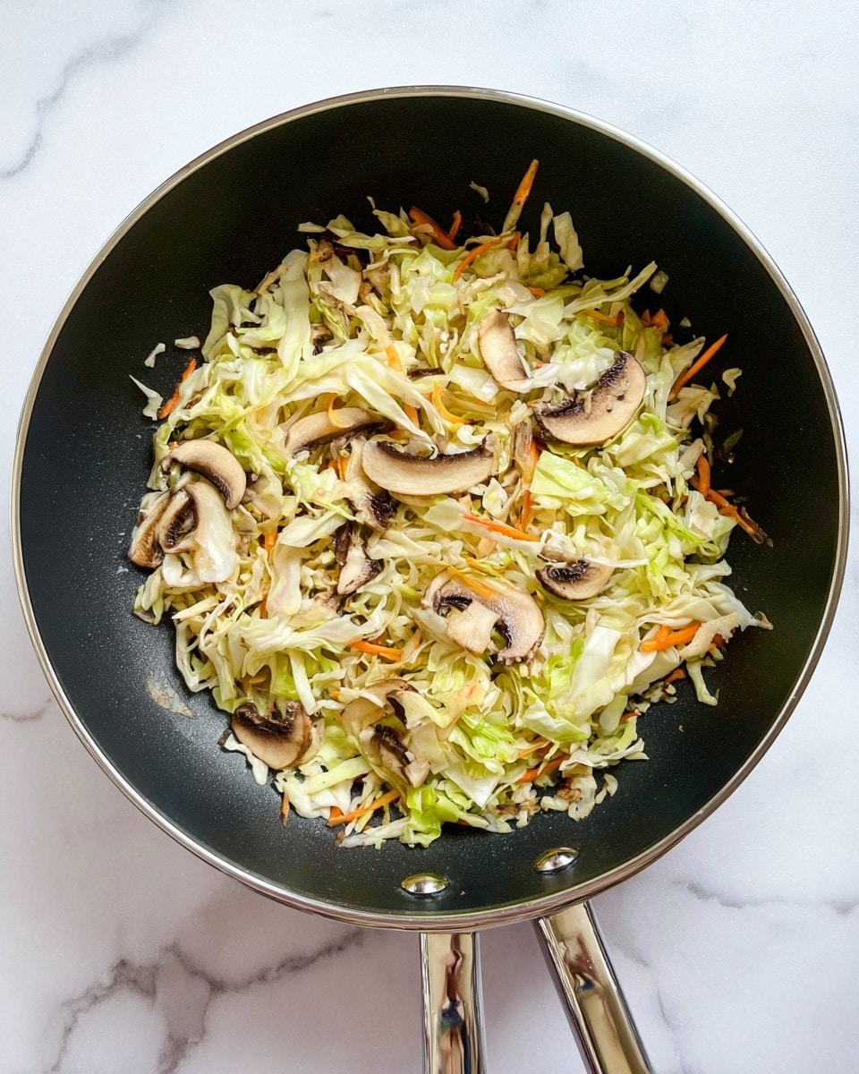 Inside a black frying pan with shiny silver handles, there is a mix of shredded cabbage, thin strips of orange carrots, and sliced brown mushrooms. The cabbage is pale green and white, making up most of the mix, while the carrots add small bright orange streaks. The mushrooms are thinly sliced and scattered evenly on top, showing their soft brown color and light edges. The pan is resting on a white marbled surface. photo taken with an iphone --ar 4:5 --v 7