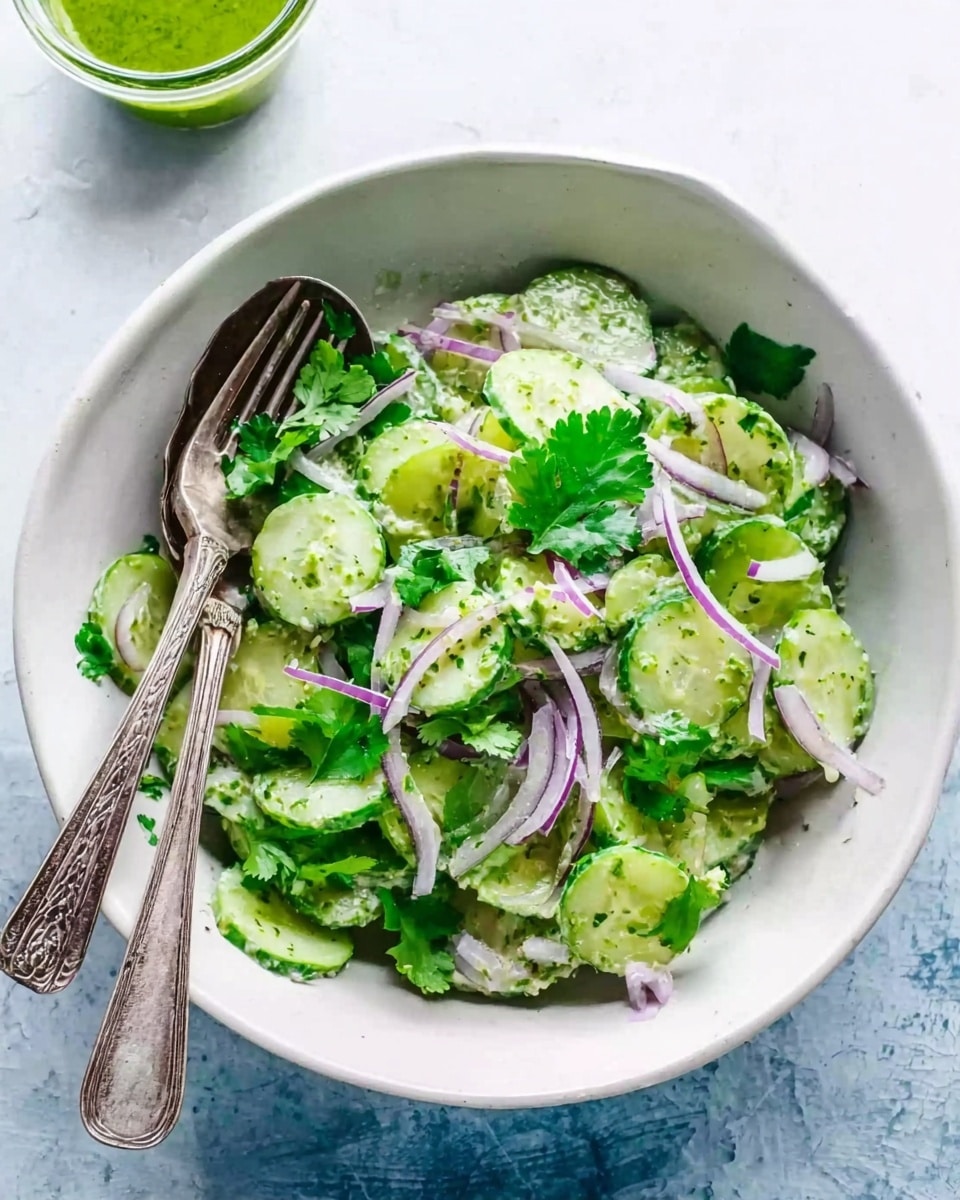 A white bowl filled with a fresh salad consisting of light green cucumber slices, thin purple onion strips, and bright green cilantro leaves scattered throughout. Two vintage silver forks rest inside the bowl on the left side, partially submerged in the salad. The bowl sits on a white marbled surface with a small glass container of green sauce or dressing slightly blurred in the background. The overall look is fresh and crisp with a mix of soft and textured elements, photo taken with an iphone --ar 4:5 --v 7