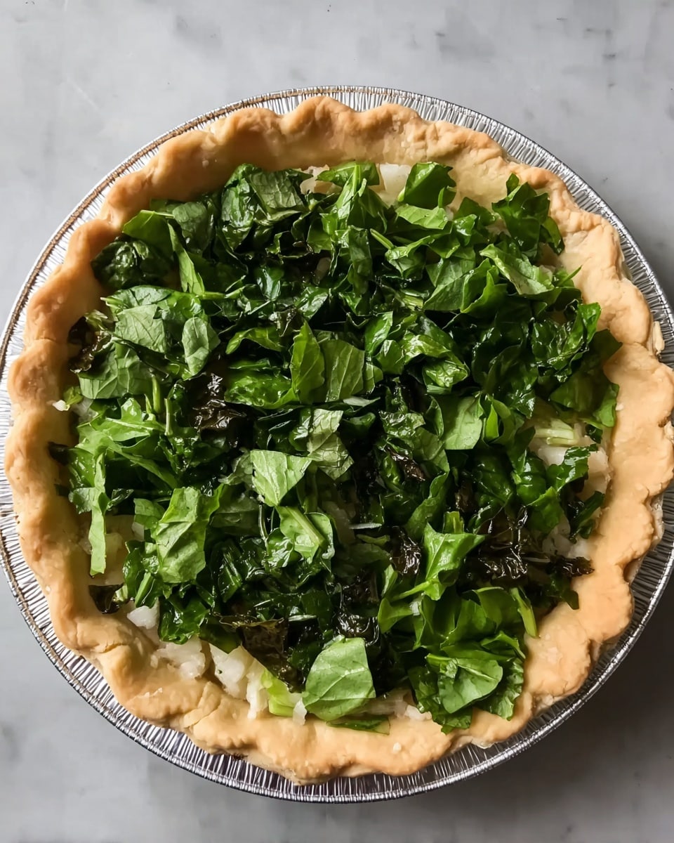 A pie with one golden, crimped crust forming the base, filled with a layer of small white pieces that look soft and light, topped with a generous amount of chopped dark and bright green leafy vegetables spread evenly across the surface. The pie is in a white pie tin, set on a white marbled surface. photo taken with an iphone --ar 4:5 --v 7