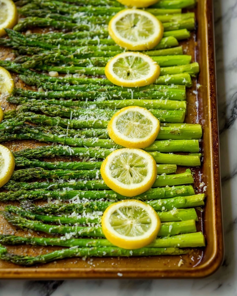 The image shows a close-up of a single layer of bright green asparagus spears laid out side by side on a textured baking sheet. The asparagus is topped with a round slice of lemon placed near the center, with light sprinkles of melted white cheese and coarse salt scattered over the spears. The asparagus tips are darker green with a slightly roasted texture. The background is a white marbled texture. photo taken with an iphone --ar 4:5 --v 7