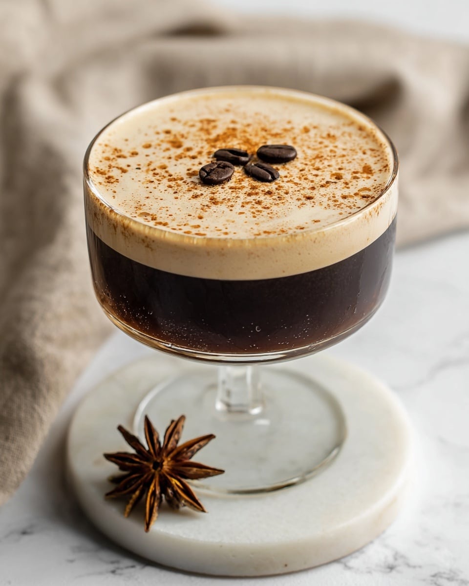 A cocktail glass with a long stem holds a two-layered drink; the bottom layer is dark brown and translucent, and the top layer is a light tan foam, smooth and thick, covering the entire surface. On the foam, there are three dark coffee beans placed near the center. The glass is set on a white marbled surface. In the background on the left side, there are two pumpkins, one white with orange stripes and one solid orange, sitting on a white textured cloth against a plain light wall. photo taken with an iphone --ar 4:5 --v 7