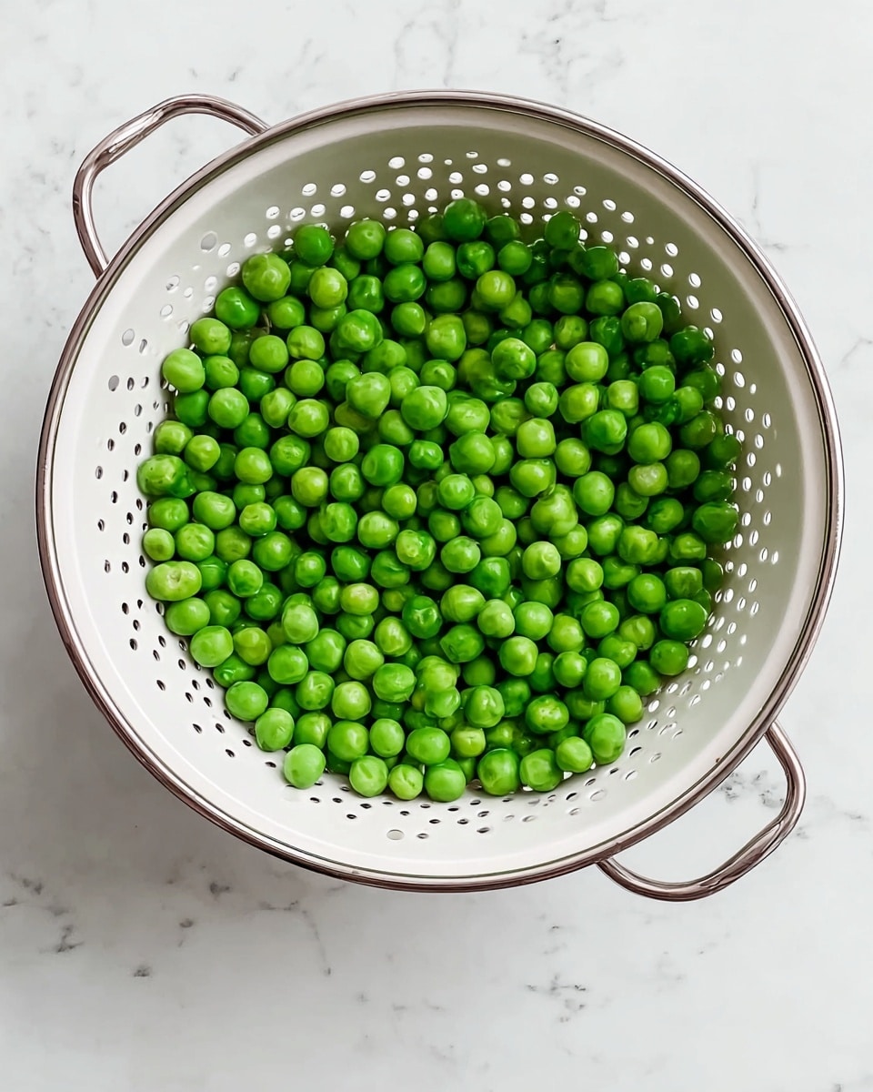 A top view of a white colander filled with a single layer of fresh, bright green peas. The colander has small round holes all around and two shiny silver handles on opposite sides. The colander sits on a white marbled surface that adds a clean and bright background to the scene. The peas are smooth and round, evenly spread inside the colander. photo taken with an iphone --ar 4:5 --v 7