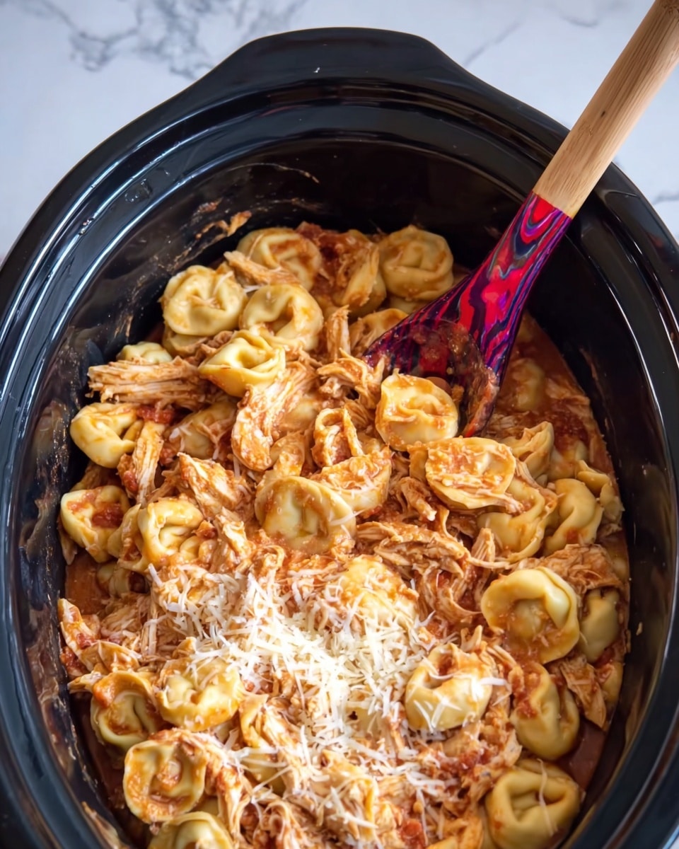 The image shows a black slow cooker filled with tortellini pasta mixed with shredded chicken and covered lightly with shredded cheese. The tortellini are light yellow with a smooth texture, and the chicken is mixed evenly, giving the dish a mix of pale yellow and light reddish-orange from the sauce. A colorful wooden spoon with red and purple swirls is placed inside the slow cooker, partially stirring the pasta. The background is a white marbled texture. photo taken with an iphone --ar 4:5 --v 7
