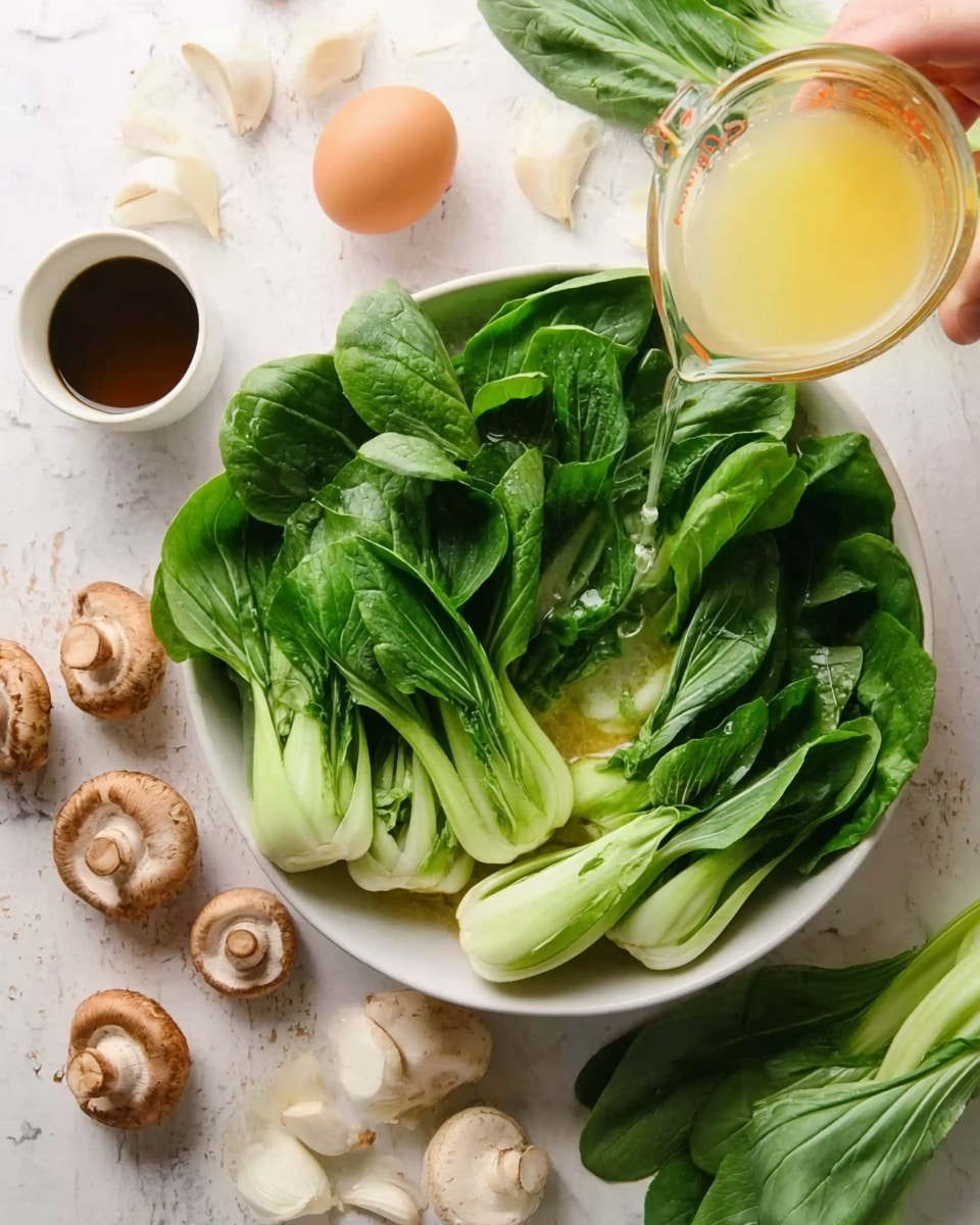 A white bowl filled with fresh green bok choy leaves neatly layered with their thick white stems at the bottom and vibrant green leaves spreading out on top. A woman's hand is pouring a light yellow liquid from a glass measuring cup over the bok choy. Around the bowl, there are whole light brown mushrooms, several white garlic cloves, an egg, and some fresh green bok choy leaves on a white marbled surface. In the top left corner, there's a small white cup with dark brown liquid. photo taken with an iphone --ar 4:5 --v 7