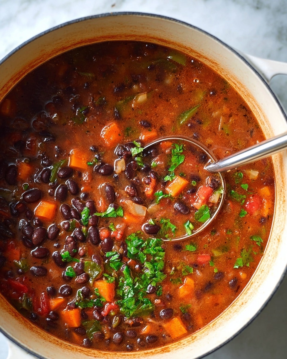 This image shows a close-up view of a large white pot filled with a thick stew made with black beans, diced orange carrots, and chopped green herbs on top, floating in a rich reddish-brown broth. The stew has visible pieces of onions and tomatoes, creating small pops of white and red color among the beans. A shiny silver ladle rests inside the pot, partially submerged in the hearty mixture. The background is a white marbled surface, adding a clean look to the scene. photo taken with an iphone --ar 4:5 --v 7