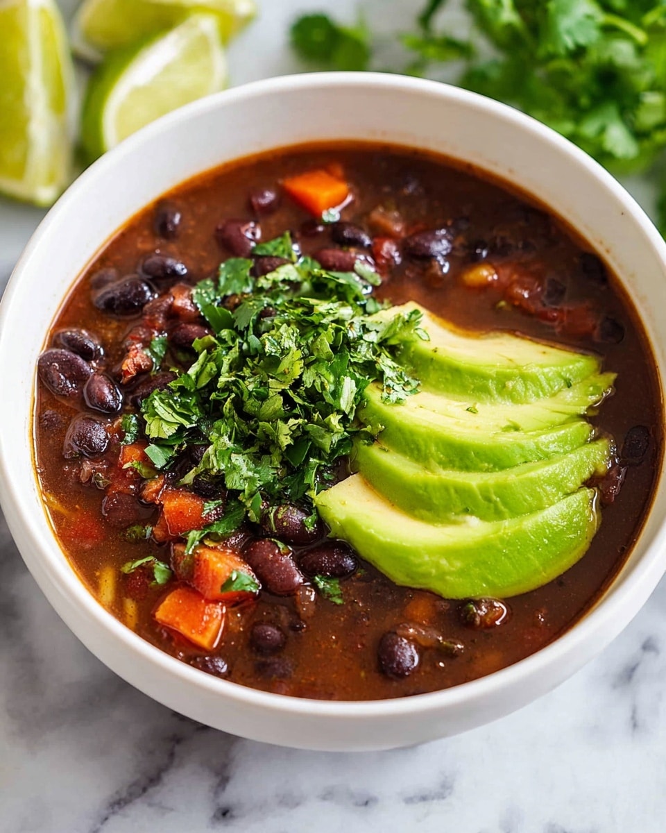 A white bowl filled with three visible layers: the bottom layer is a rich, dark brown broth with whole black beans and small pieces of orange carrot all mixed in, the middle layer has bright fresh green cilantro leaves scattered on top, and the top layer shows several thick slices of vibrant green avocado, neatly placed on one side. The bowl sits on a white marbled surface with some blurred green herbs and lime wedges in the background. photo taken with an iphone --ar 4:5 --v 7