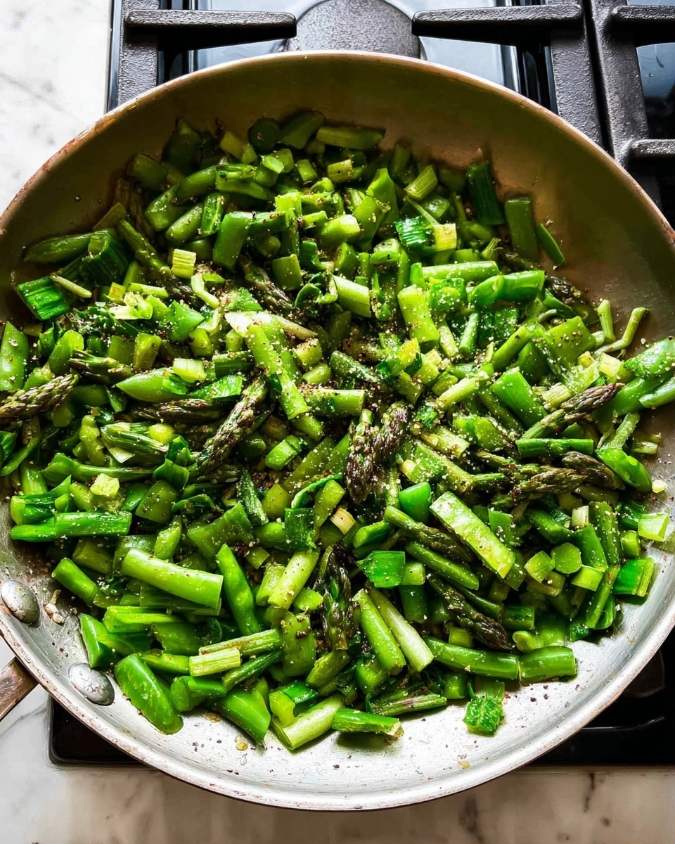 A metal pan filled with chopped green vegetables, mainly snap peas and asparagus cut into small pieces, showing different shades of green and some textured edges. The vegetables have a light sprinkle of black pepper and some salt visible on top. The pan is on a gas stove with dark burners and metallic parts around it, placed on a white marbled surface. The image looks bright and fresh, capturing the textures and colors clearly. photo taken with an iphone --ar 4:5 --v 7