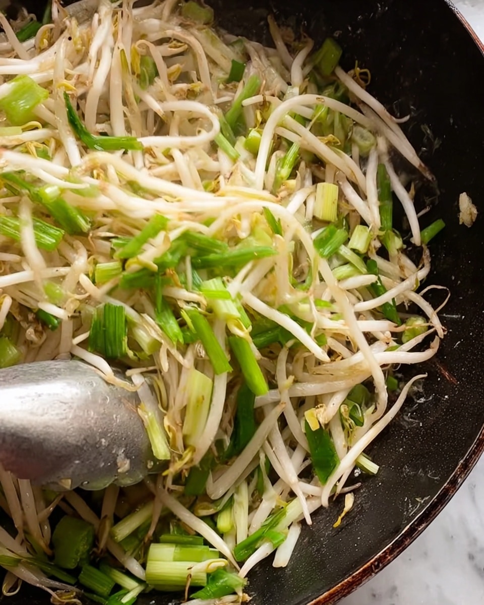 The image shows a close-up of bean sprouts and chopped green onions cooking together. The bean sprouts are thin and white with slight browning, mixed with fresh, light green onion pieces cut into small sections. The ingredients are inside a black pan, and a woman's hand holding a metal cooking utensil is seen stirring the vegetables. The background is a white marbled texture. photo taken with an iphone --ar 4:5 --v 7