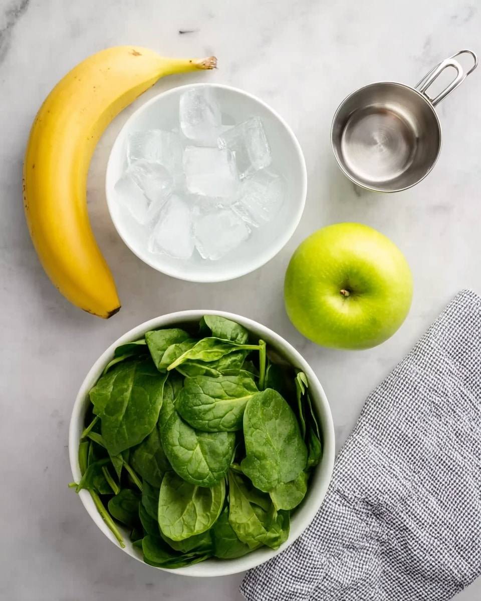 The image shows a white marble surface with a fresh yellow banana placed at the top left. Below the banana is a white bowl filled with several ice cubes, giving a clear and cool look. To the right of the ice bowl, there is a small metal measuring cup with a handle, showing a clean shiny texture. Below the measuring cup, a bright green apple sits on the marble surface, its smooth skin reflecting light. Finally, at the bottom left corner of the image, a white bowl is full of fresh, vibrant green spinach leaves, layered loosely with different sizes and shapes of leaves. A gray and white cloth napkin is partially visible on the right edge of the image. Photo taken with an iphone --ar 4:5 --v 7