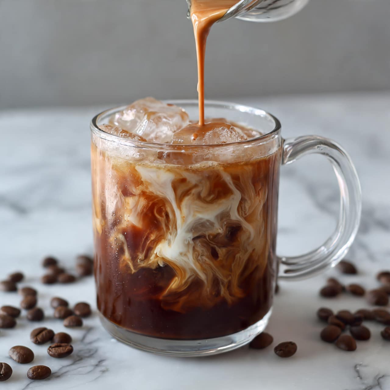 A clear glass mug with a handle is filled with ice and cold coffee, creating a dark brown layer at the top and a lighter brown layer in the middle. A creamy liquid is being poured from above into the glass, swirling into the coffee and blending the colors with soft swirling patterns. The mug is set on a white marbled surface with scattered whole coffee beans around it. Photo taken with an iphone --ar 4:5 --v 7