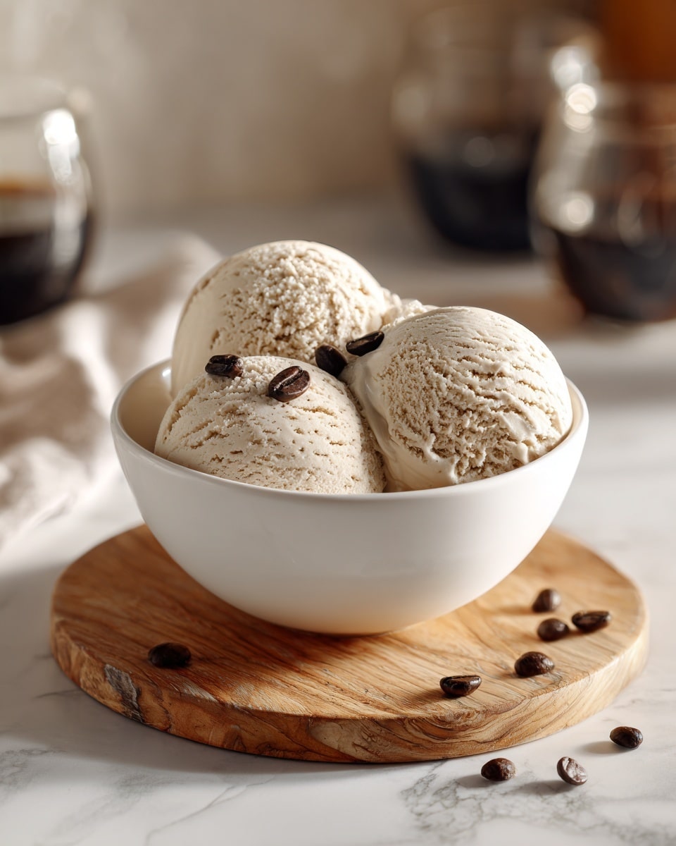 A white bowl filled with three rounded scoops of light beige ice cream, each scoop showing a creamy and slightly textured surface. Small dark coffee beans are scattered on and around the ice cream, adding contrast. The bowl sits on a round wooden board with natural grain details, all set on a white marbled surface. The background is softly blurred, showing glass and metal objects creating a cozy, warm atmosphere. photo taken with an iphone --ar 4:5 --v 7