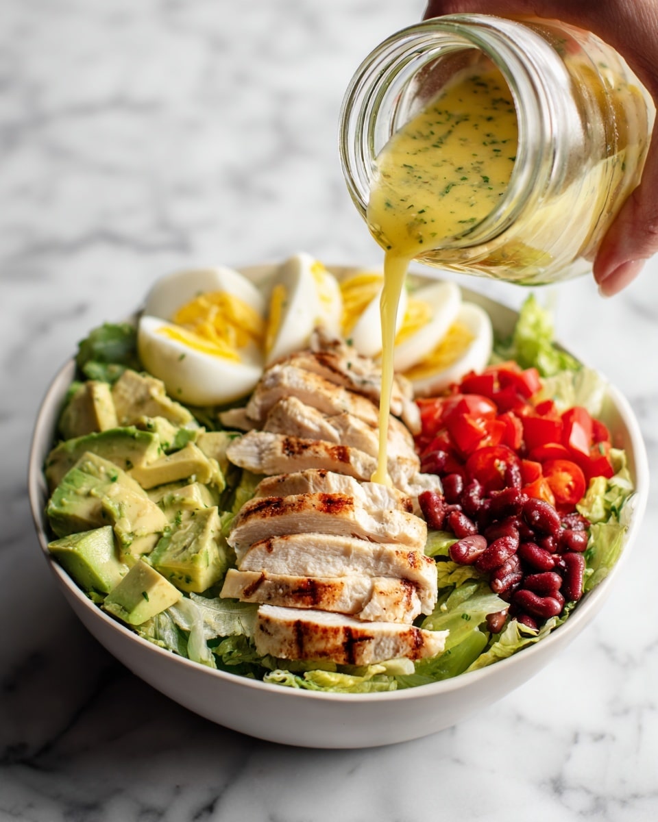 A white bowl filled with a layered salad is shown, starting with a base of green lettuce at the bottom. On top of the lettuce, there are sliced grilled chicken pieces with light brown grill marks, arranged in the center. Around the chicken, there are avocado slices with a creamy light green color placed on the left side, halved hard-boiled eggs with bright yellow yolks on the bottom right, small diced red tomatoes on the right side, and some darker red beans next to the tomatoes. A woman's hand is holding a small jar tilted over the bowl, pouring a yellow dressing with green herb flecks over the salad. The background and surface are white marble. Photo taken with an iphone --ar 4:5 --v 7