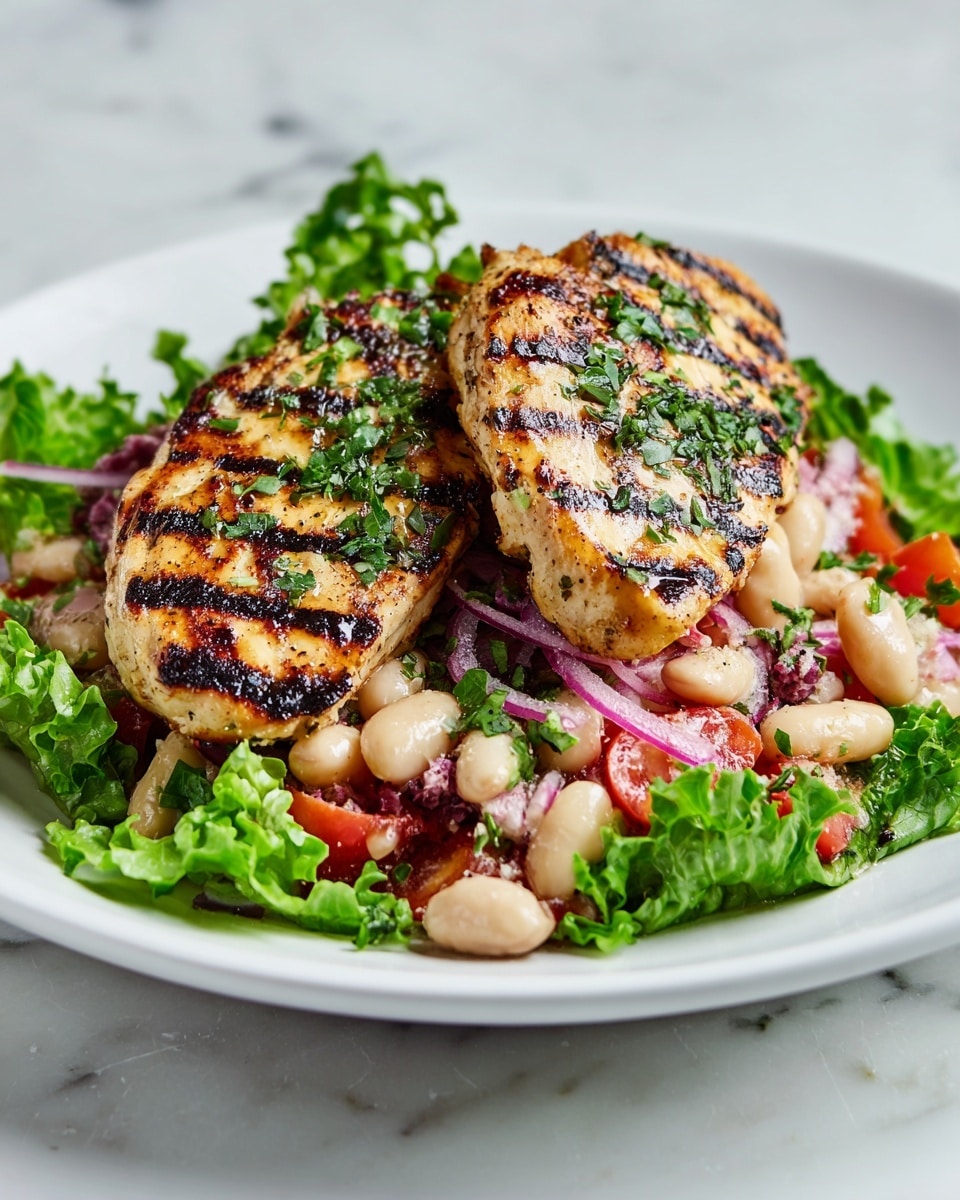 The dish shows two grilled chicken pieces with dark grill marks and chopped green herbs on top, placed in the center of a white plate. Underneath, there is a mix of chopped red cherry tomatoes, white beans, and thin slices of purple onion spread all over. The edges of the plate are lined with fresh green lettuce leaves that add a bright color to the dish. The plate is placed on a white marbled surface. photo taken with an iphone --ar 4:5 --v 7