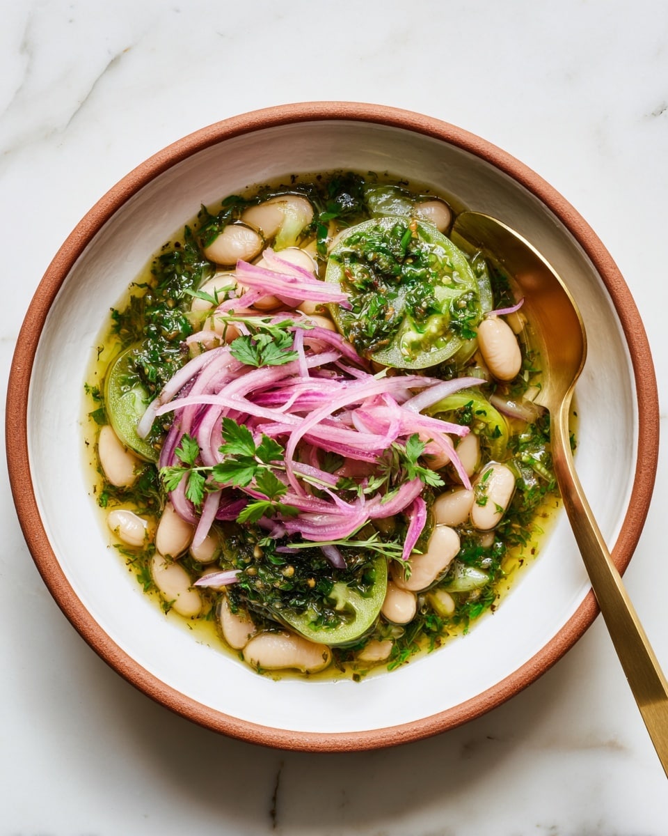 A white bowl with a brown rim holds a dish starting with a light green sauce or broth covering white beans. On top of the beans there is a layer of thin red onion rings and slices of green cucumbers. The dish is finished with fresh green herbs scattered on top. A shiny golden spoon is placed inside the bowl on the right side. The bowl sits on a white marbled surface. photo taken with an iphone --ar 4:5 --v 7