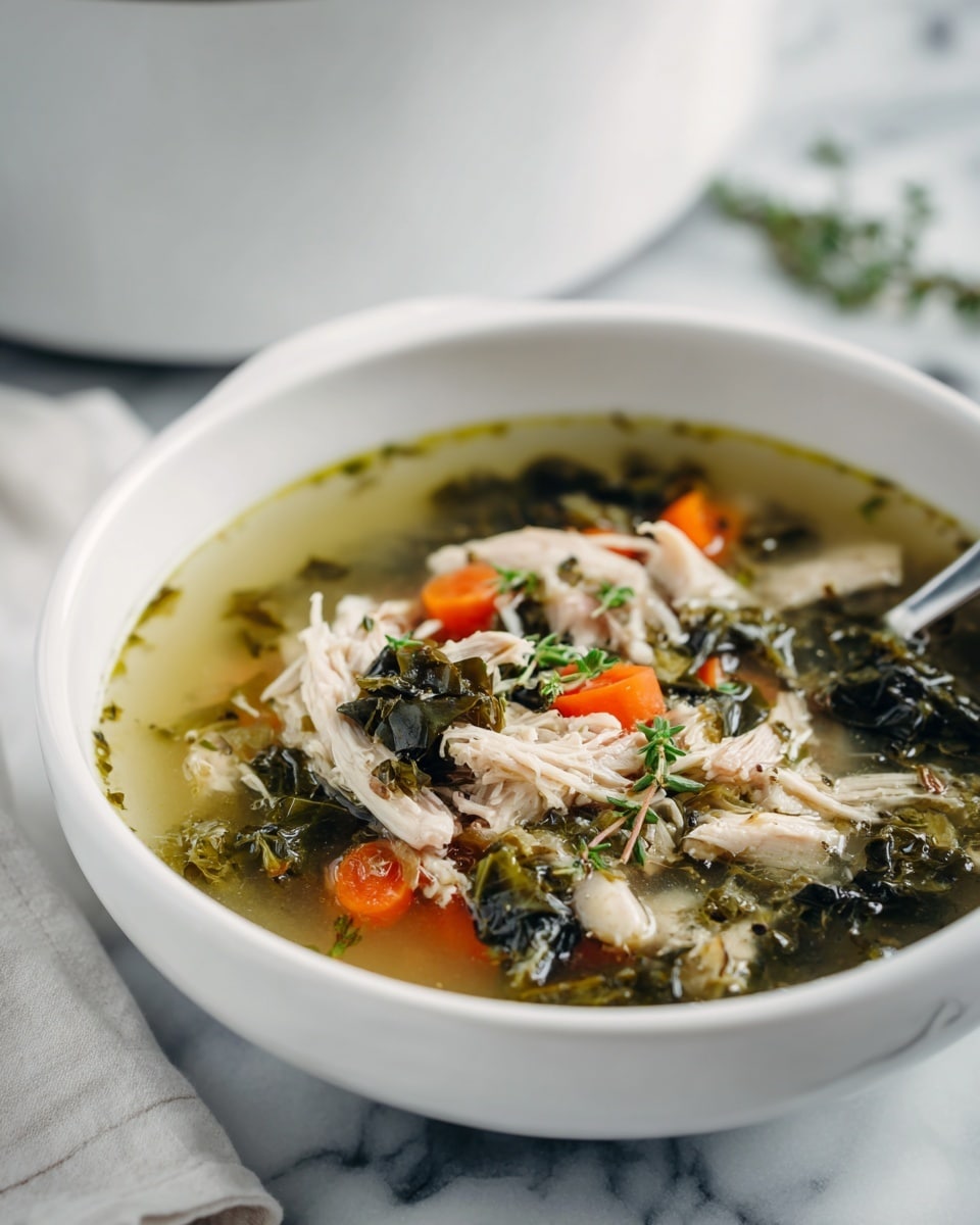 A white bowl filled with a clear broth soup that has several layers visible: the base is a light yellow-green liquid with small bits of herbs floating in it, above that are pieces of shredded white meat, dark green leafy vegetables, and chunks of bright orange carrot scattered throughout. There are small green herb sprigs sprinkled on top, adding texture and color contrast. The bowl is placed on a white marbled surface, and in the blurry background, a white pot can be seen. Photo taken with an iphone --ar 4:5 --v 7