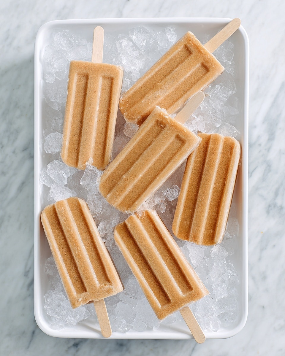 There are six light brown popsicles with smooth surfaces and grooves on one side, arranged on crushed ice inside a white tray. The popsicles have wooden sticks partly visible at the top, and the ice crystals around them sparkle against a white marbled texture background. The tray sits on a white marbled surface, making the scene look fresh and cool. photo taken with an iphone --ar 4:5 --v 7