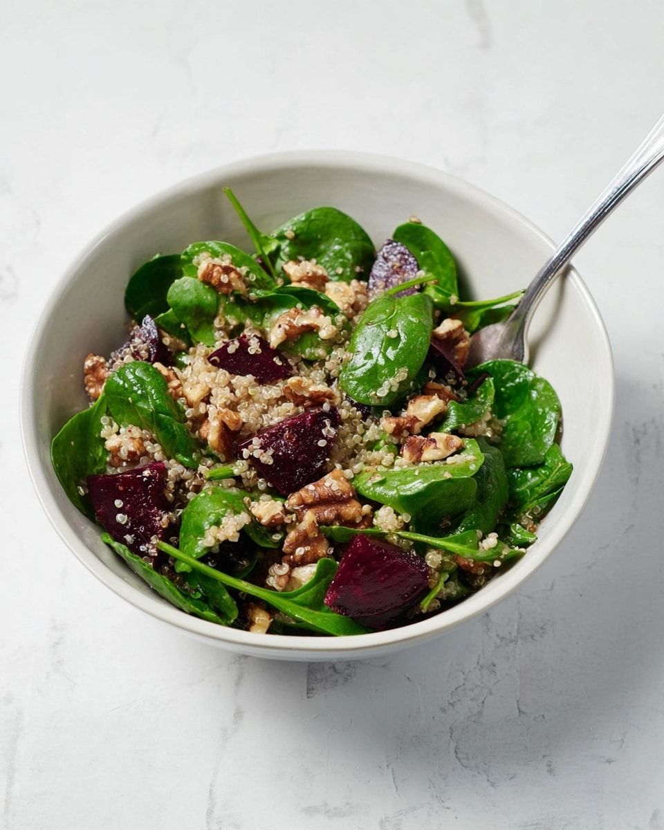 A white bowl with a salad sits on a white marbled surface. The salad has three main layers: at the bottom, small, light beige quinoa grains; above that, dark purple beet pieces and bright green spinach leaves spread all over, adding fresh and rich color; on top, brown crunchy nut clusters scattered unevenly, giving a rough texture. Some bits of light dressing are visible over the salad. A silver fork is placed inside the bowl, resting on the right side. Photo taken with an iphone --ar 4:5 --v 7