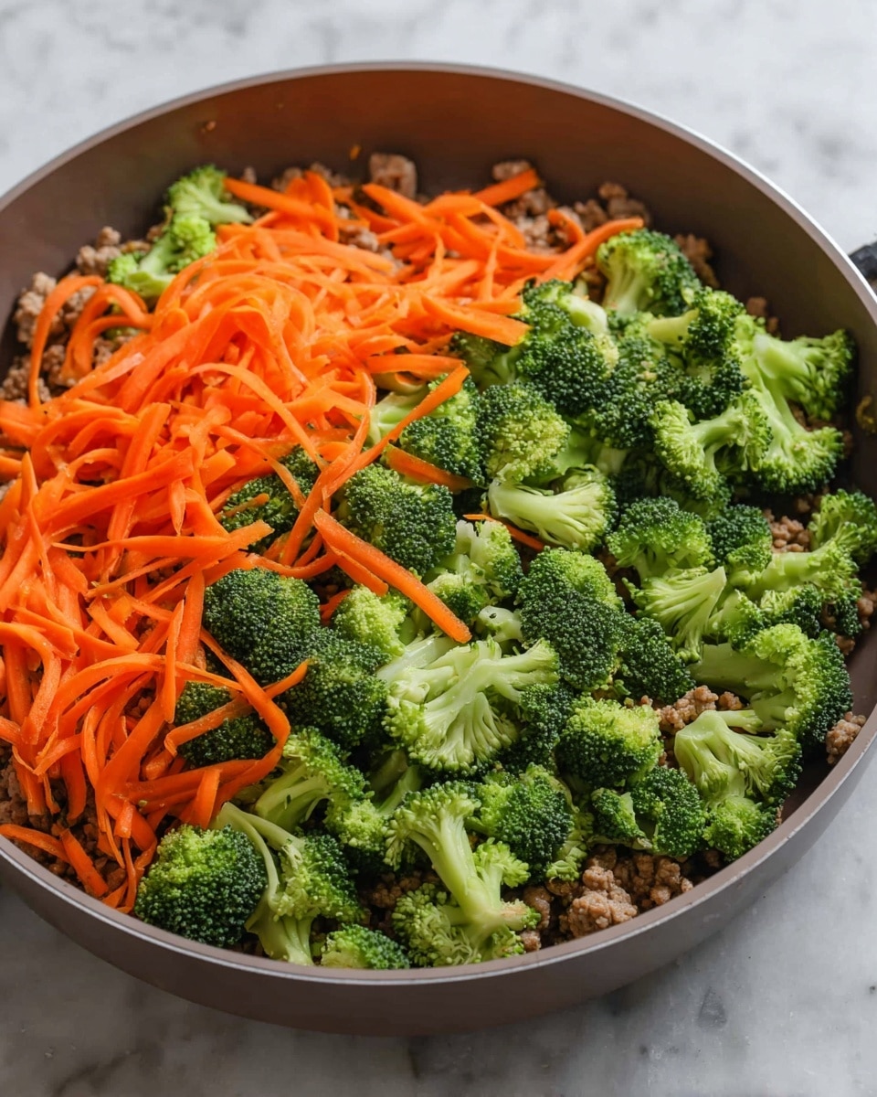 A gray pan filled with three visible layers: the bottom layer is cooked ground meat in a light brown color, the middle layer is fresh bright green broccoli florets scattered evenly, and the top layer consists of thin, long orange carrot strips spread across the broccoli. The pan sits on a white marbled surface. photo taken with an iphone --ar 4:5 --v 7
