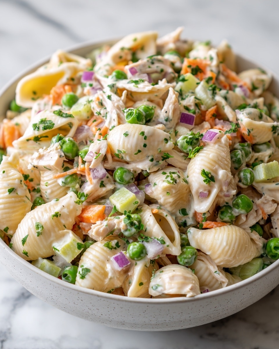 The dish shows a close-up view of a pasta salad in a white bowl on a white marbled texture. The salad has four main layers: the first layer contains light beige shell pasta with a smooth texture filling most of the bowl, mixed throughout with pieces of pale cooked chicken strips spread evenly. The second layer shows bright green peas scattered all over, adding pops of green. The third layer includes thin orange carrot sticks and small green celery cubes mixed evenly. The fourth layer has tiny purple onion cubes scattered on top, covered lightly with a creamy white dressing flecked with small green herbs. The photo is taken with an iphone --ar 4:5 --v 7