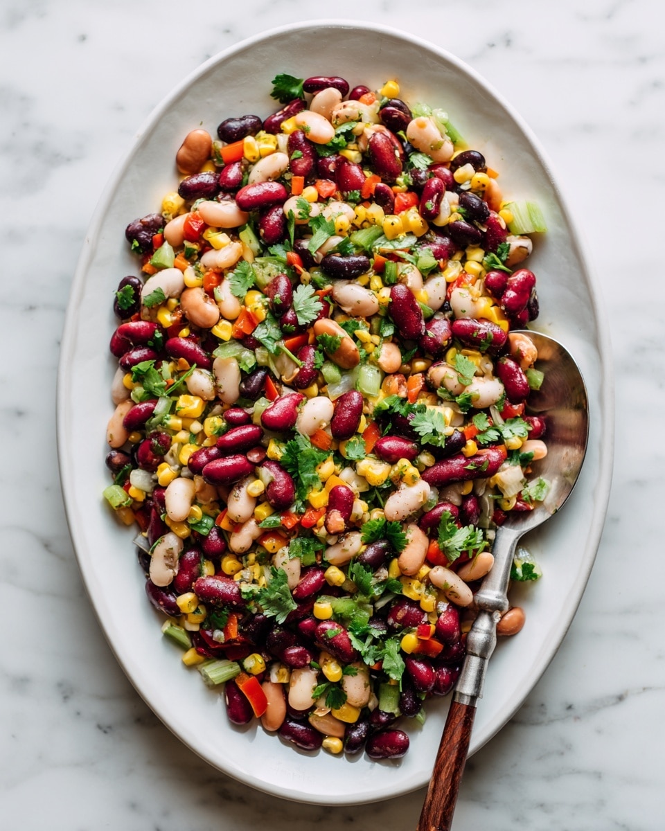 A white oval plate is filled with a colorful bean salad showing many types of beans in red, white, black, and beige on top with yellow corn scattered all over. There are small pieces of green celery and fresh cilantro leaves mixed throughout, giving a fresh and vibrant feel. On the right side of the plate, a wooden spoon with a silver handle is resting on the edge, partly inside the salad. The whole plate sits on a white marbled surface. photo taken with an iphone --ar 4:5 --v 7